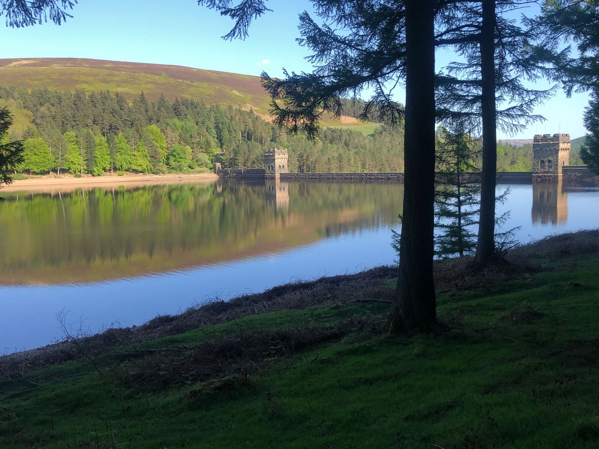 Picturesque dam on the reservoir, surrounded by green hills under blue skies.