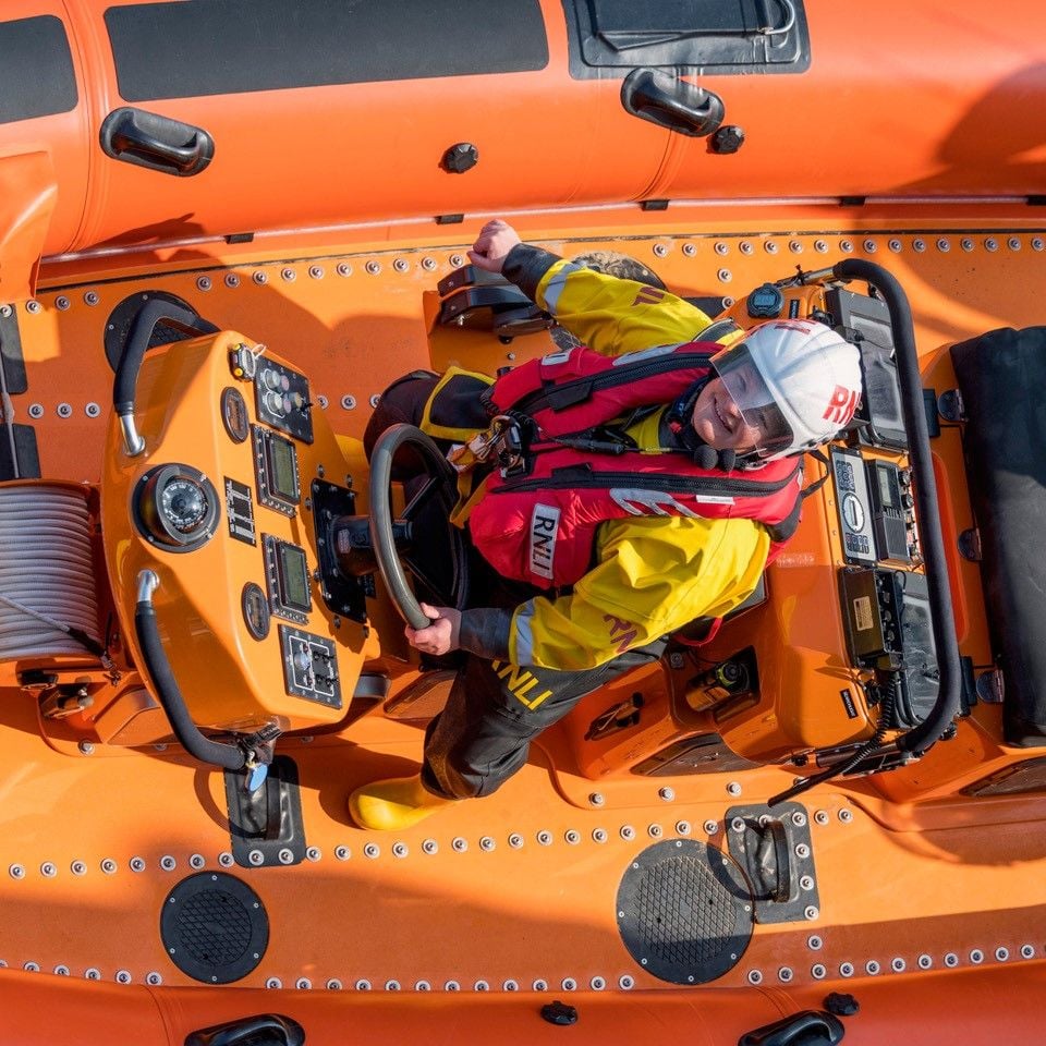Woman steering an RNLI lifeboat wearing full safety gear.