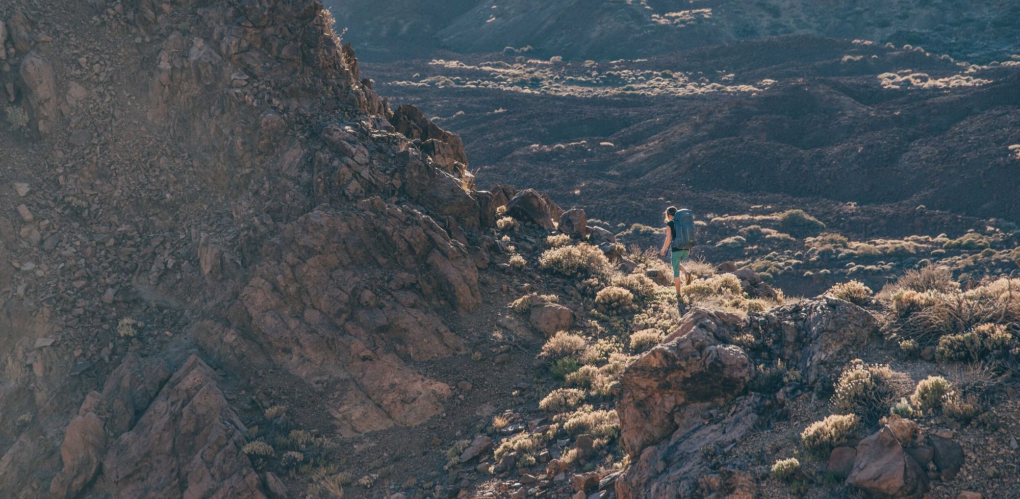 A female hiker walking across an arid landscape.