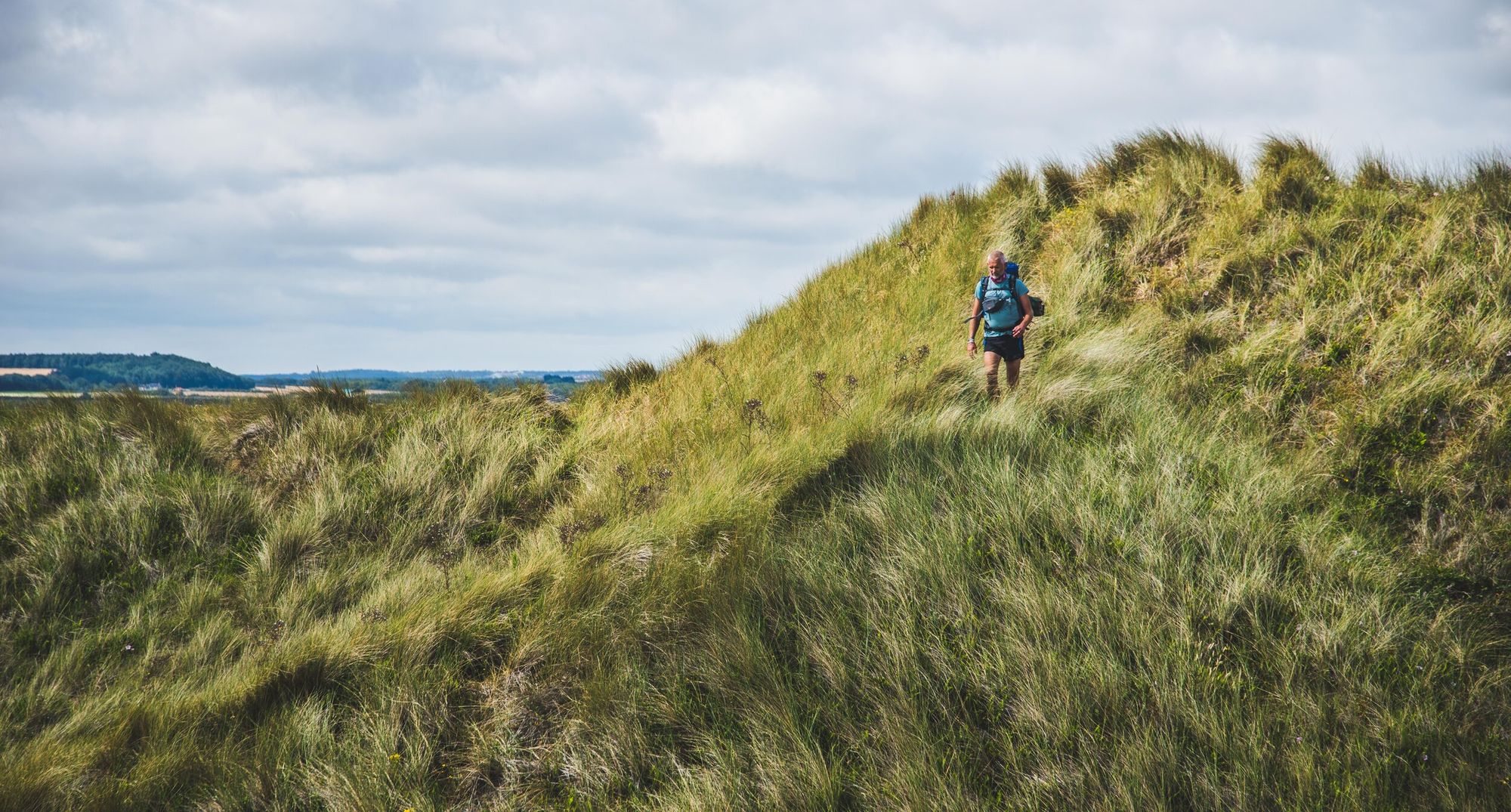 A male hiker walking through hilly grasslands.