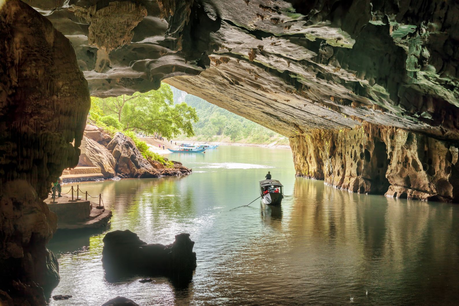A scenic view of the Son River from Phong Nha Cave in Vietnam. A tourist boat sails out of the wet cave.