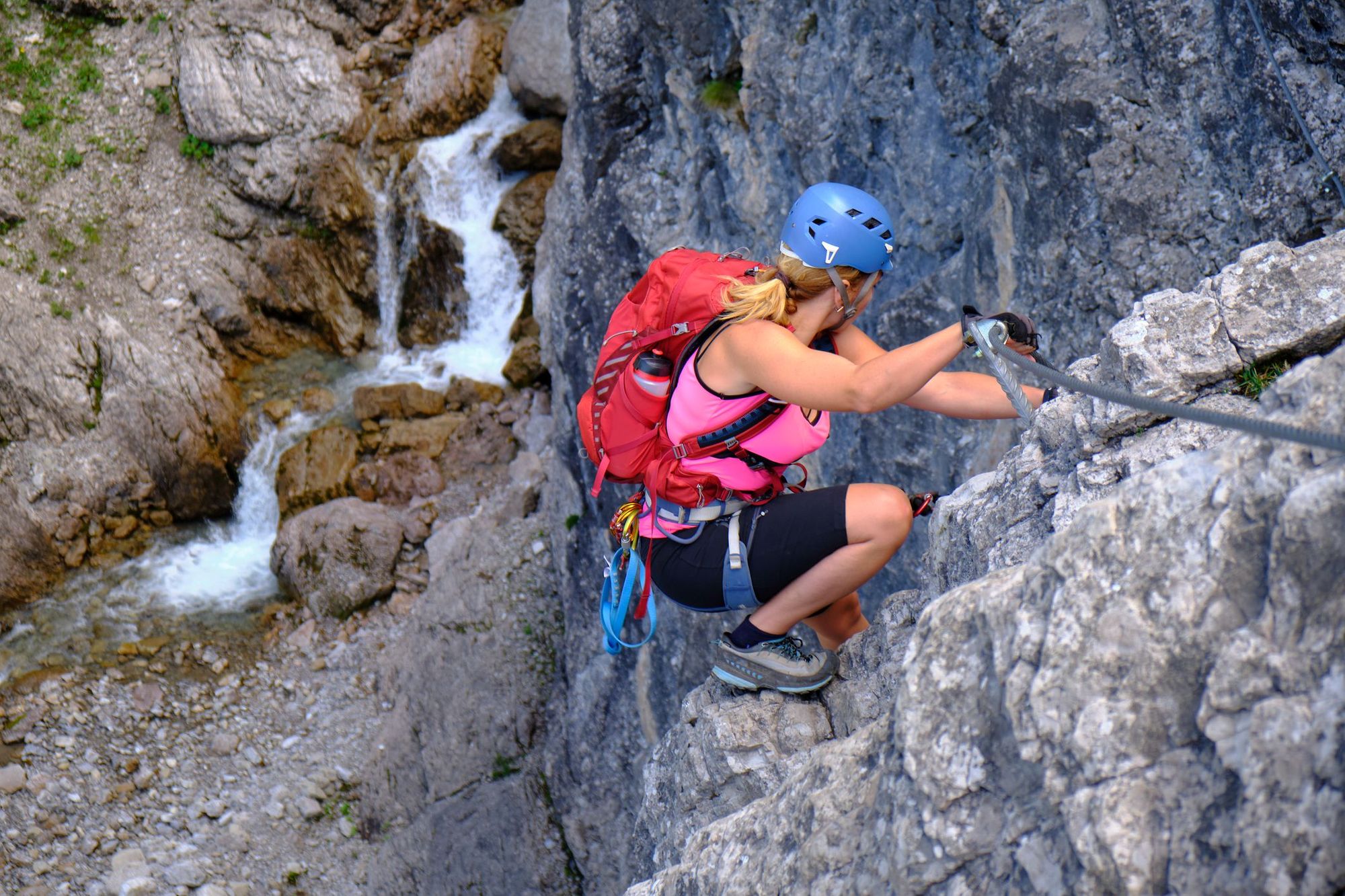 A woman climbing a via ferrata in the Australian Tirol, near a waterfall.