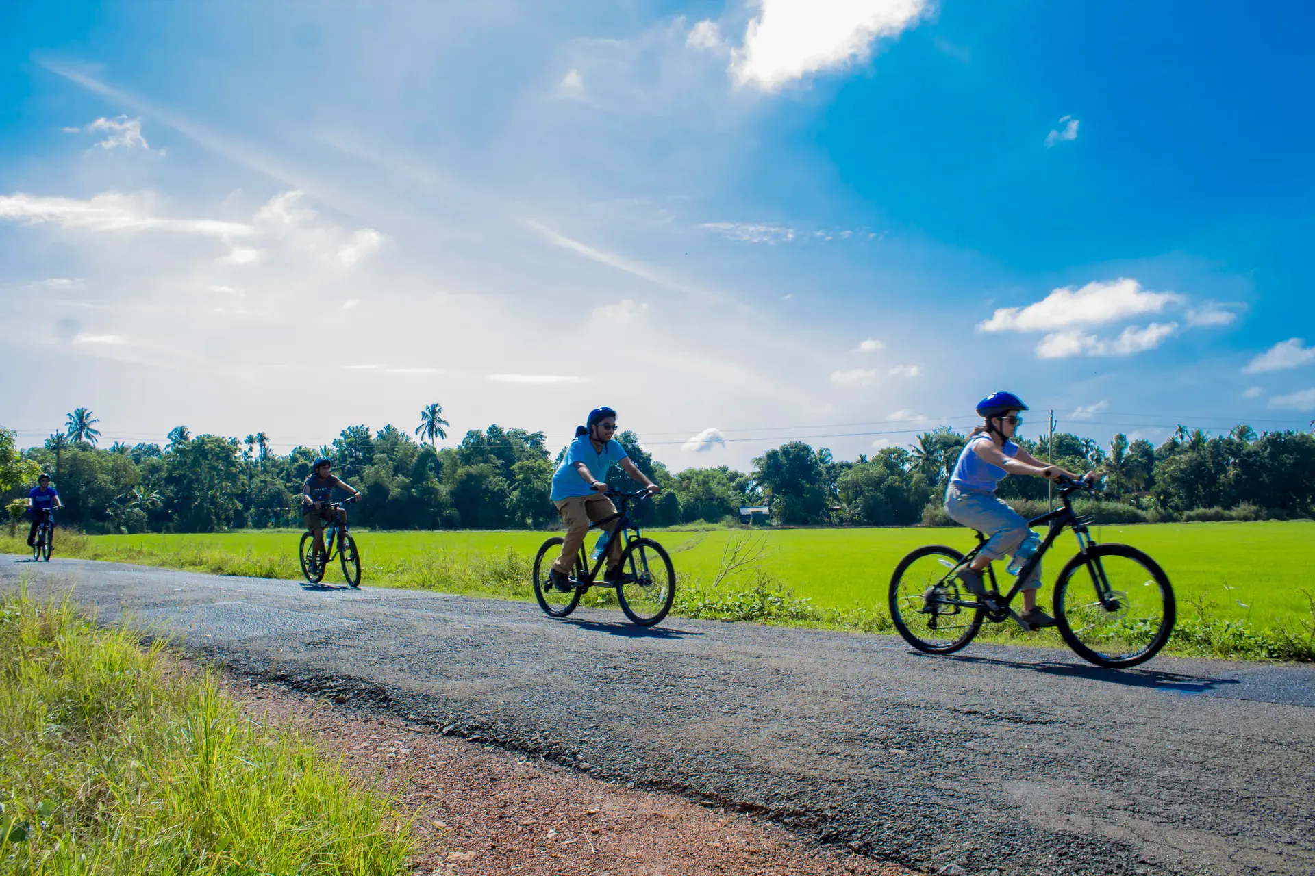 Cyclists on a tarmacked track pedalling through lush green landscape in Kerala