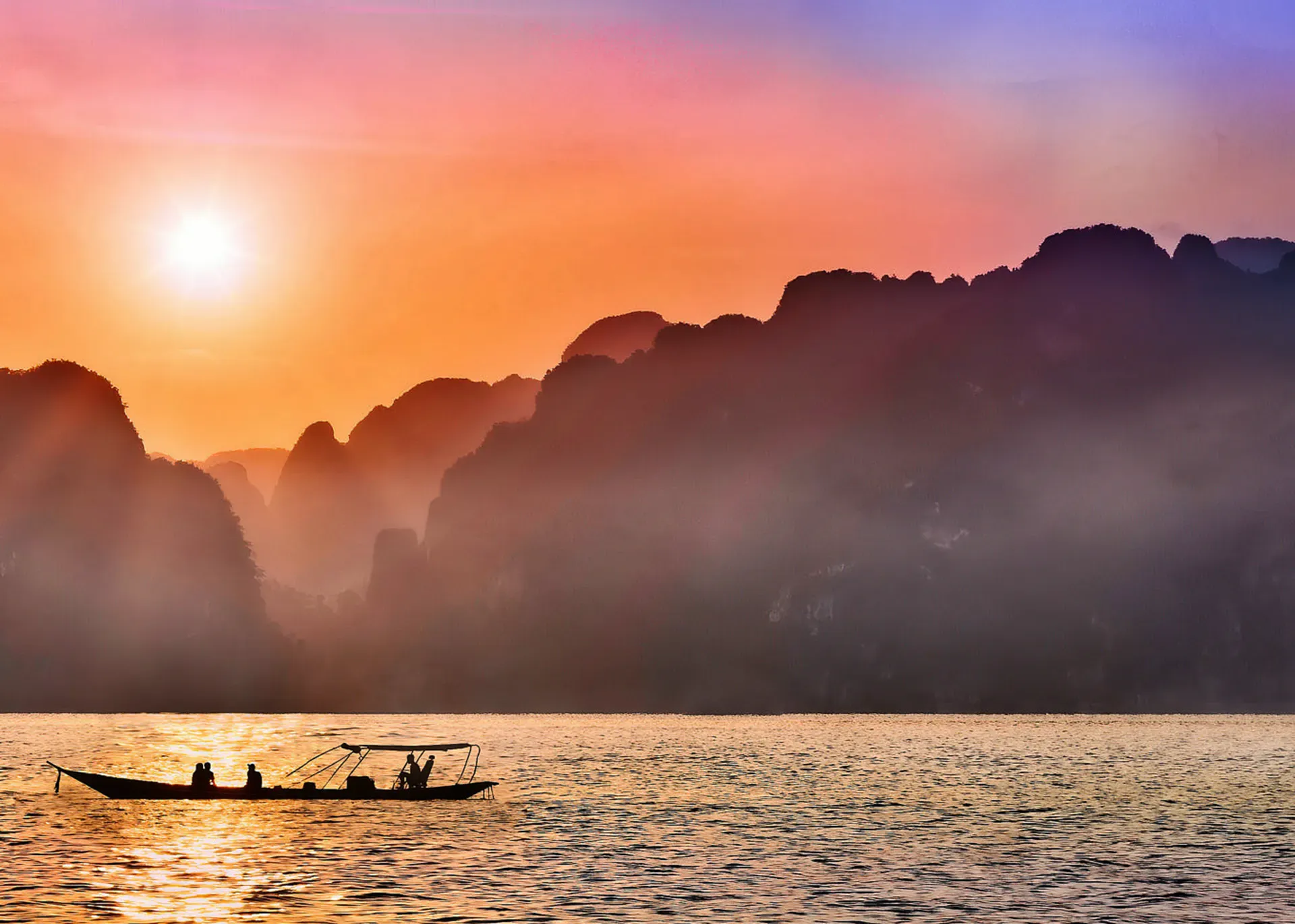 Sunset behind the karst towers of Thailand's seas with a boat silhouetted in the foreground.