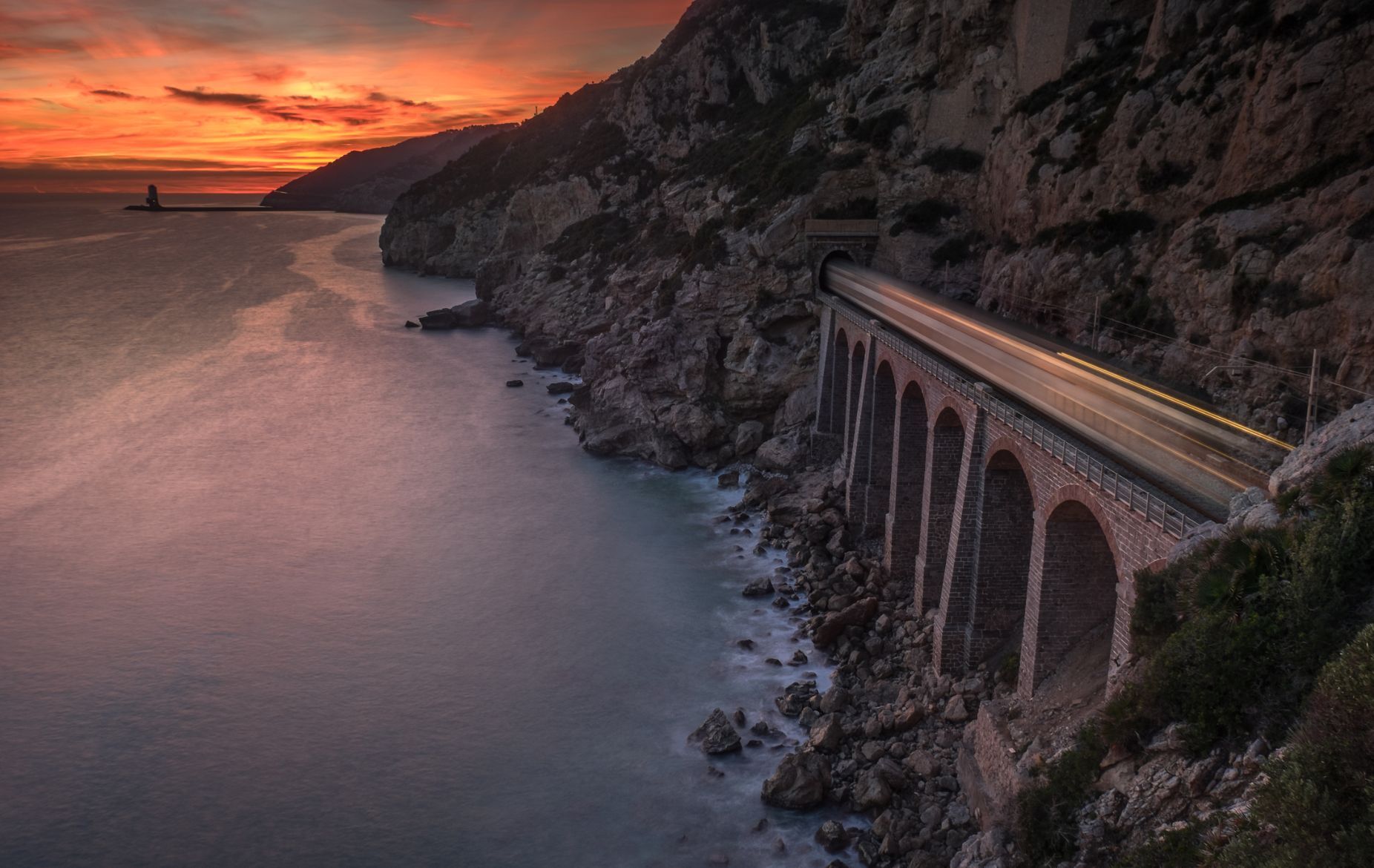 Sunset on the shores of the Garraf, of the province of Barcelona, with the sea, cliffs and the train passing through a bridge that runs along the coast between tunnels.