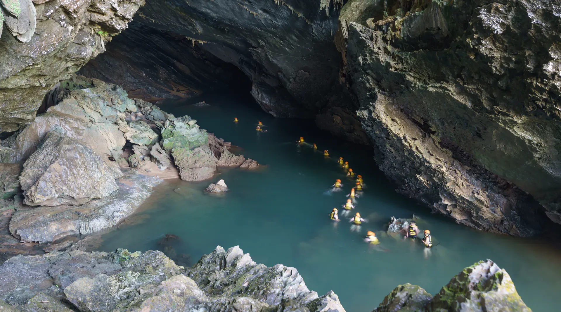 A string of people swimming into the dramatic Tra Ang Cave, Vietnam