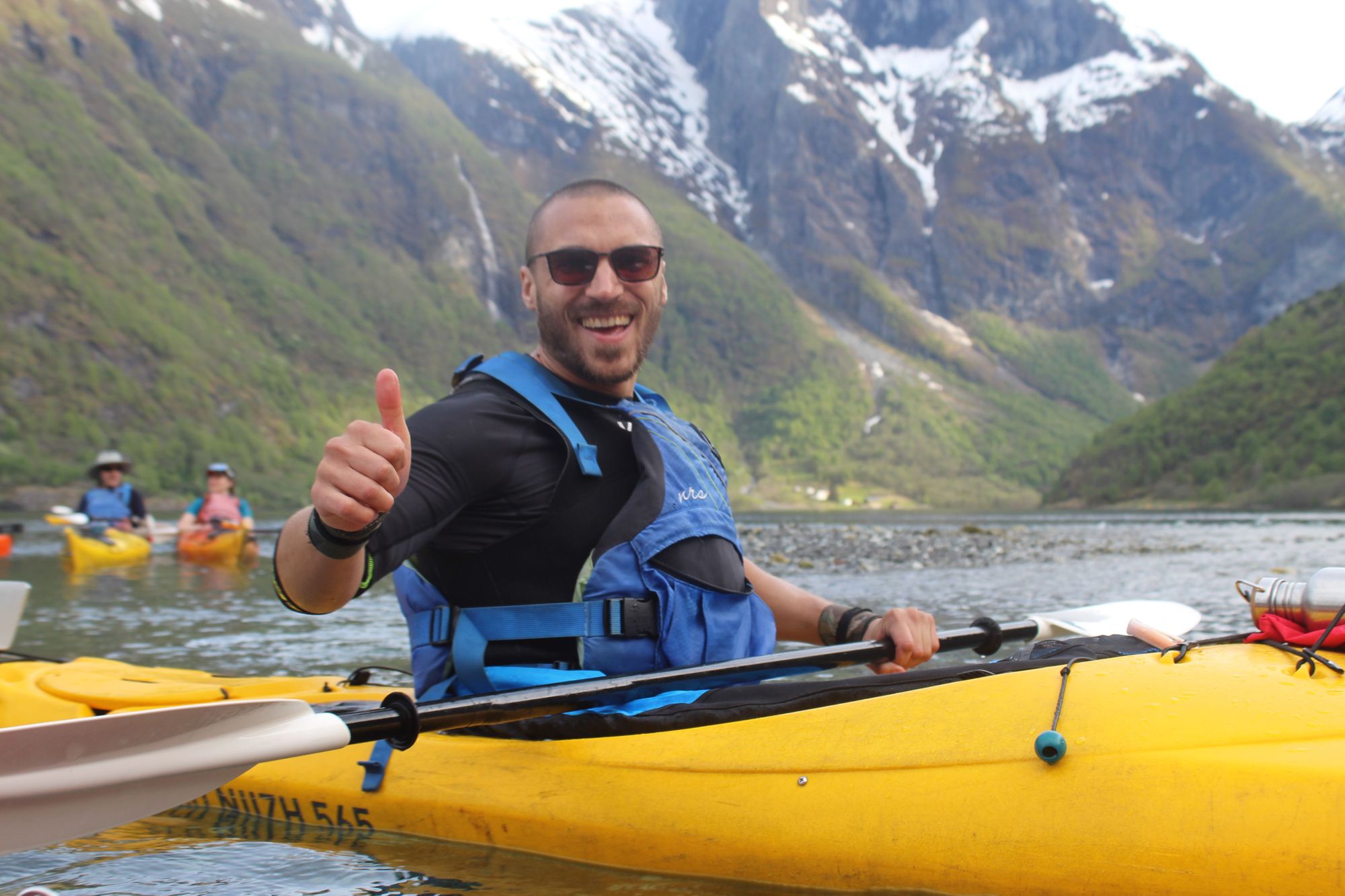 A man poses with his thumb up on a kayak in the Norwegian fjords.