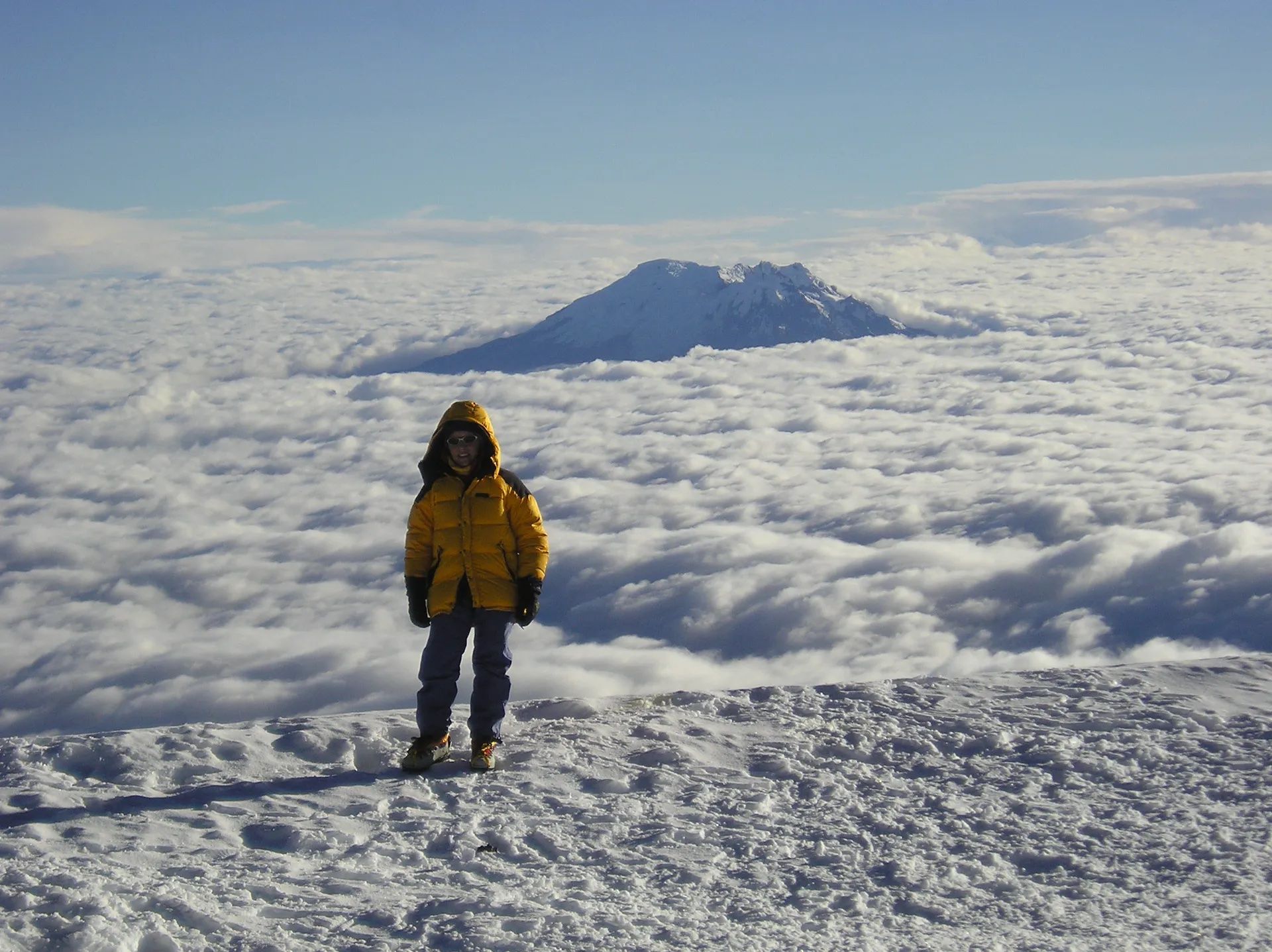 A climber standing on the summit of Cotopaxi Volcano, with a sea of clouds behind them.