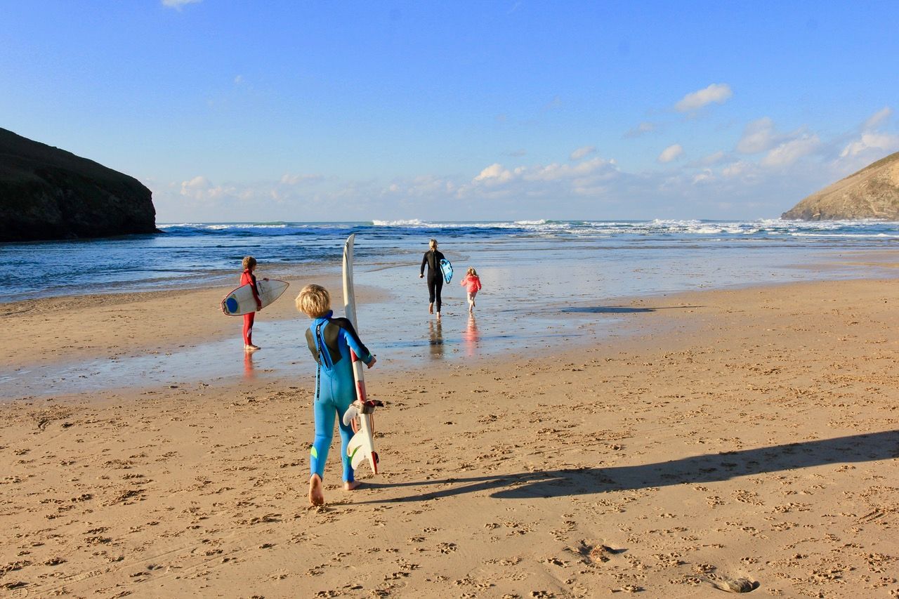 Three children carry their surfboards to the beach, following their mother.