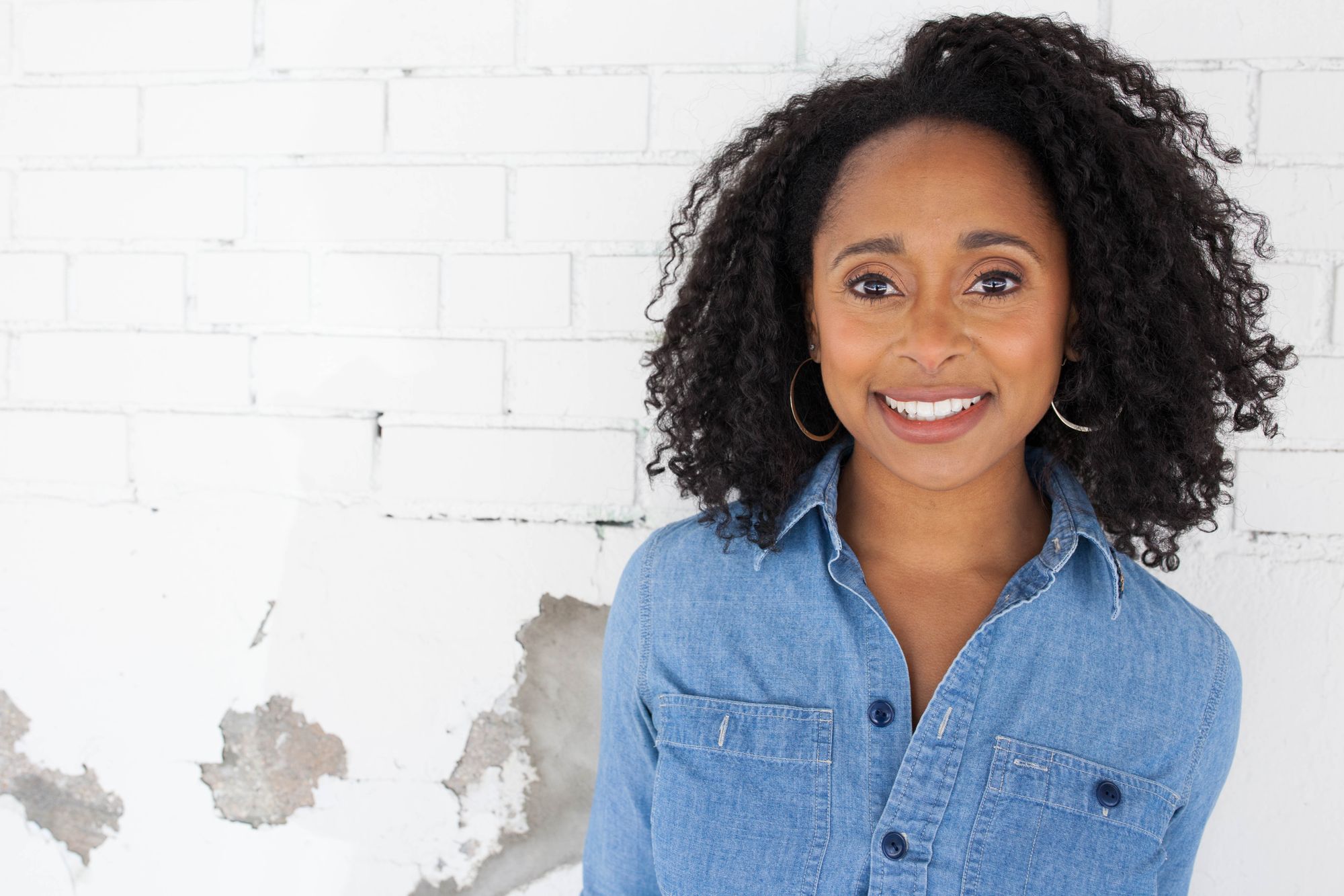 The ecologist Dr. Rae Wynn-Grant, host of the Going Wild podcast, in front of a white wall.