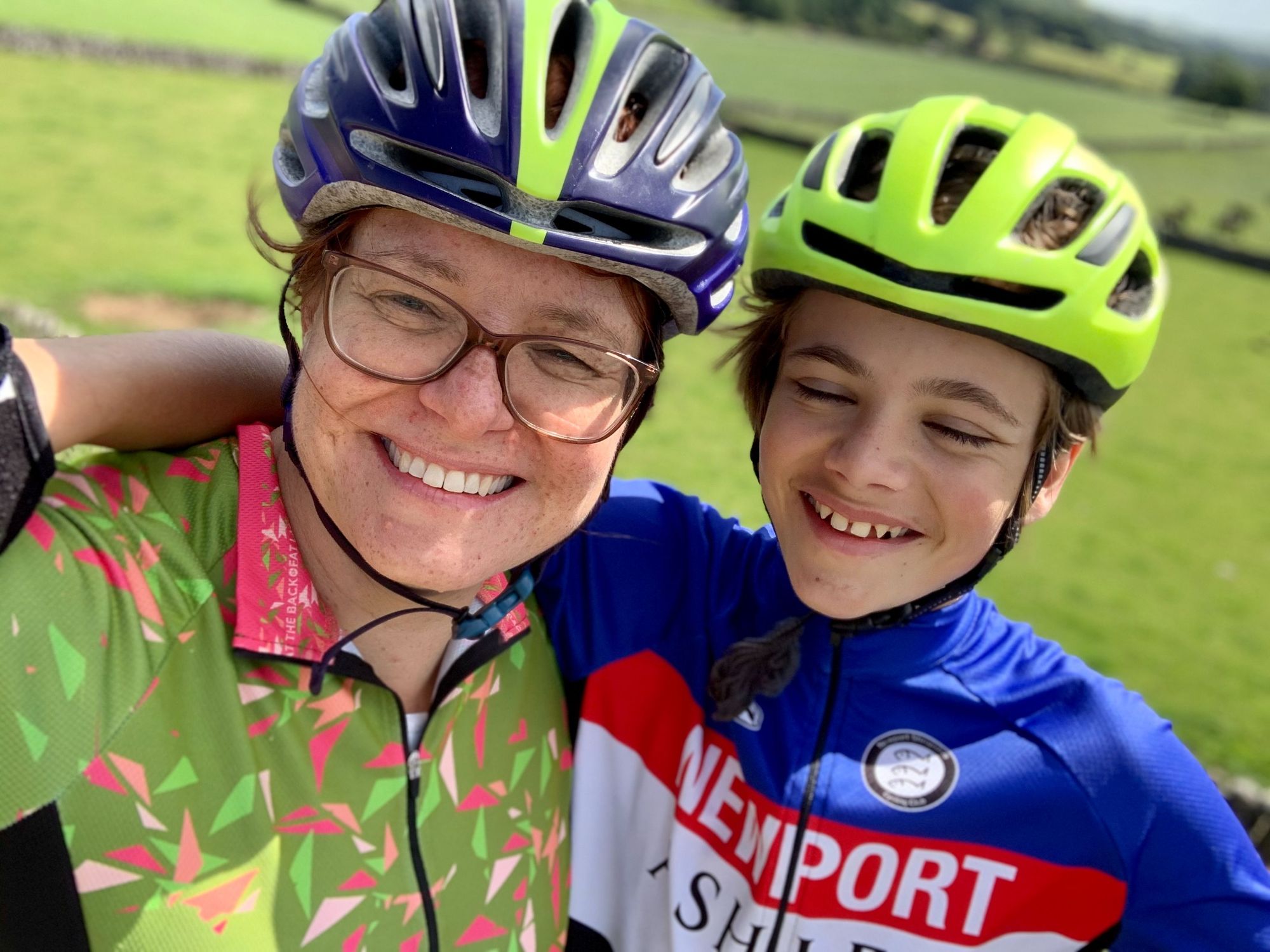 A female cyclist poses with her young son, both dressed in cycling gear.