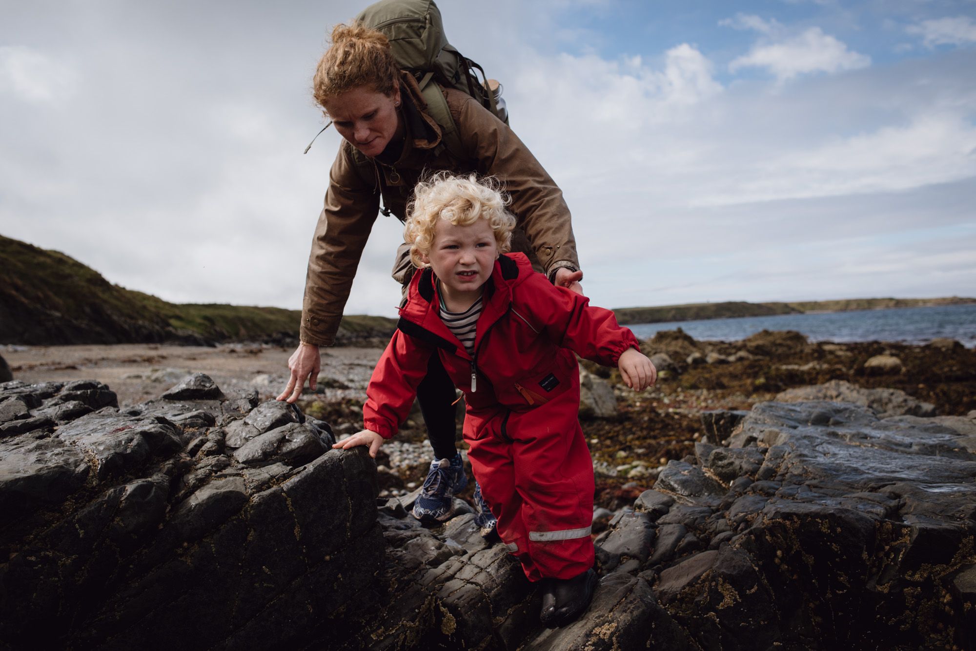 A woman hiking across the shoreline, with her child in front of her.