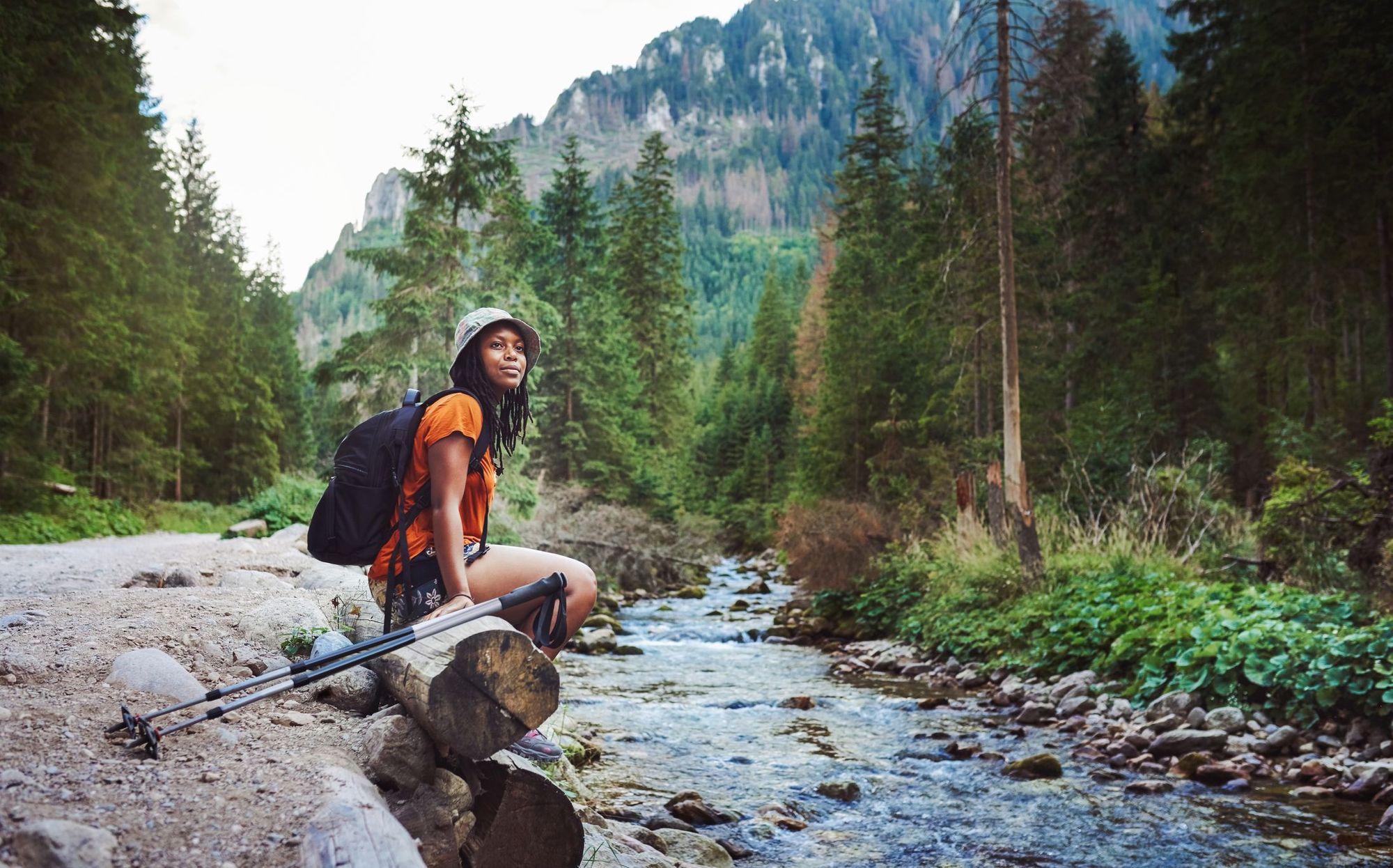 A woman hiker sits on a log by a river, listening quietly
