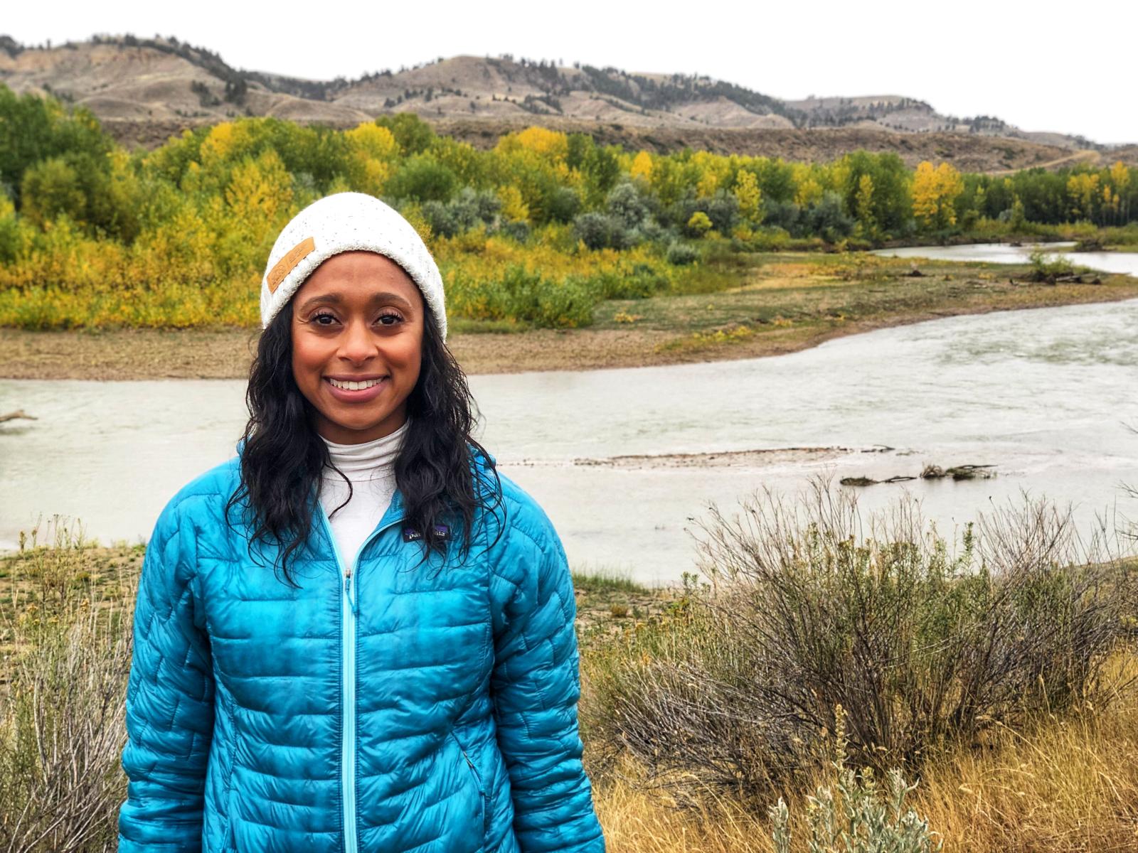 The ecologist Dr. Rae Wynn-Grant standing in front of a river and some hills.