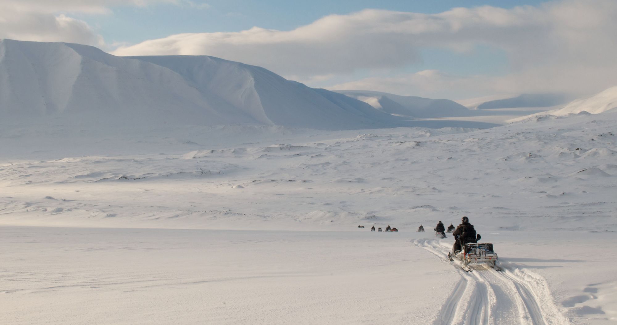 A snowmobile expedition travels across the snowy landscape of Svalbard.
