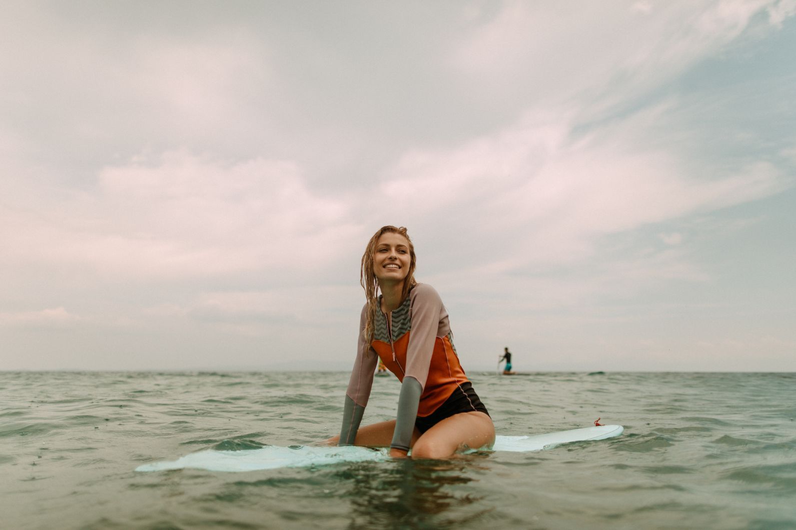 A smiling woman sits on a surfboard in the sea.