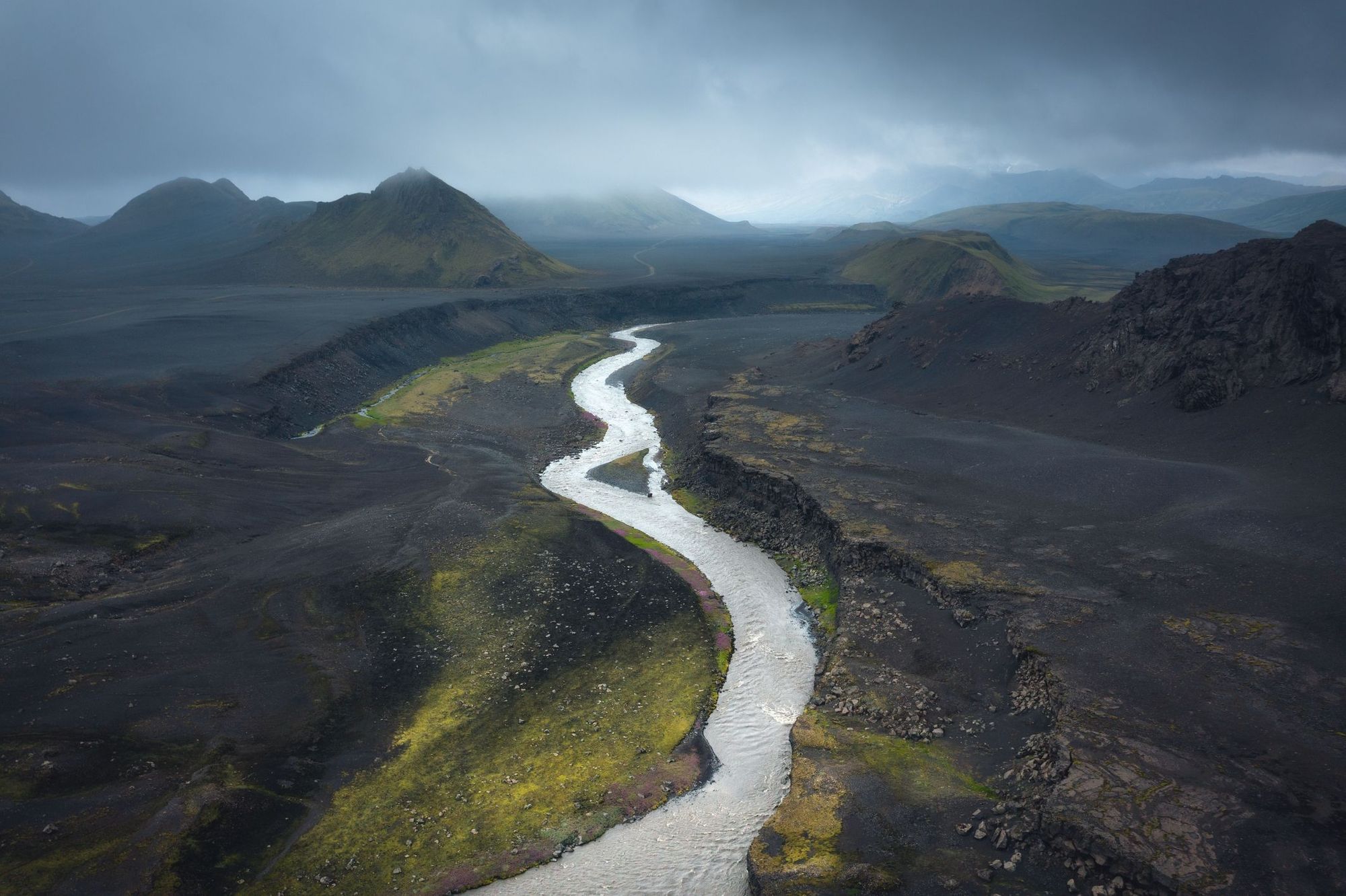 A river carving through black lava fields on the Laugavegur Trail in Iceland shows