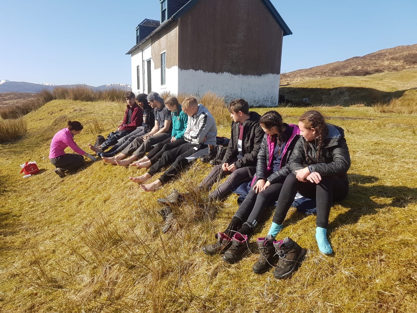 An expedition medic examines teenage participants' feet in the Scottish Highlands.