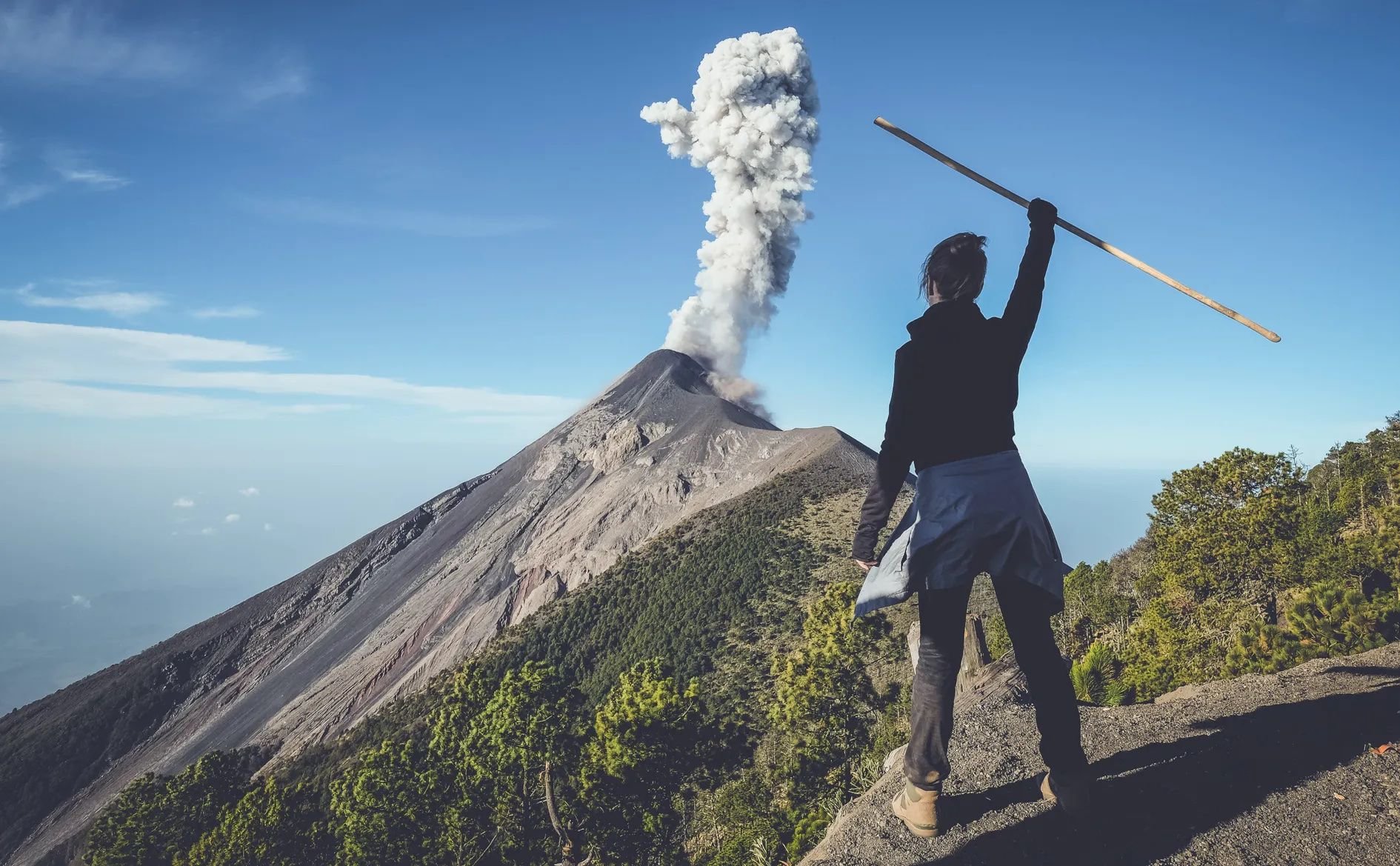 A hiker stands on the summit of Santa Maria volcano in Guatemala, looking out at an eruption from nearby Santiaguito summit.