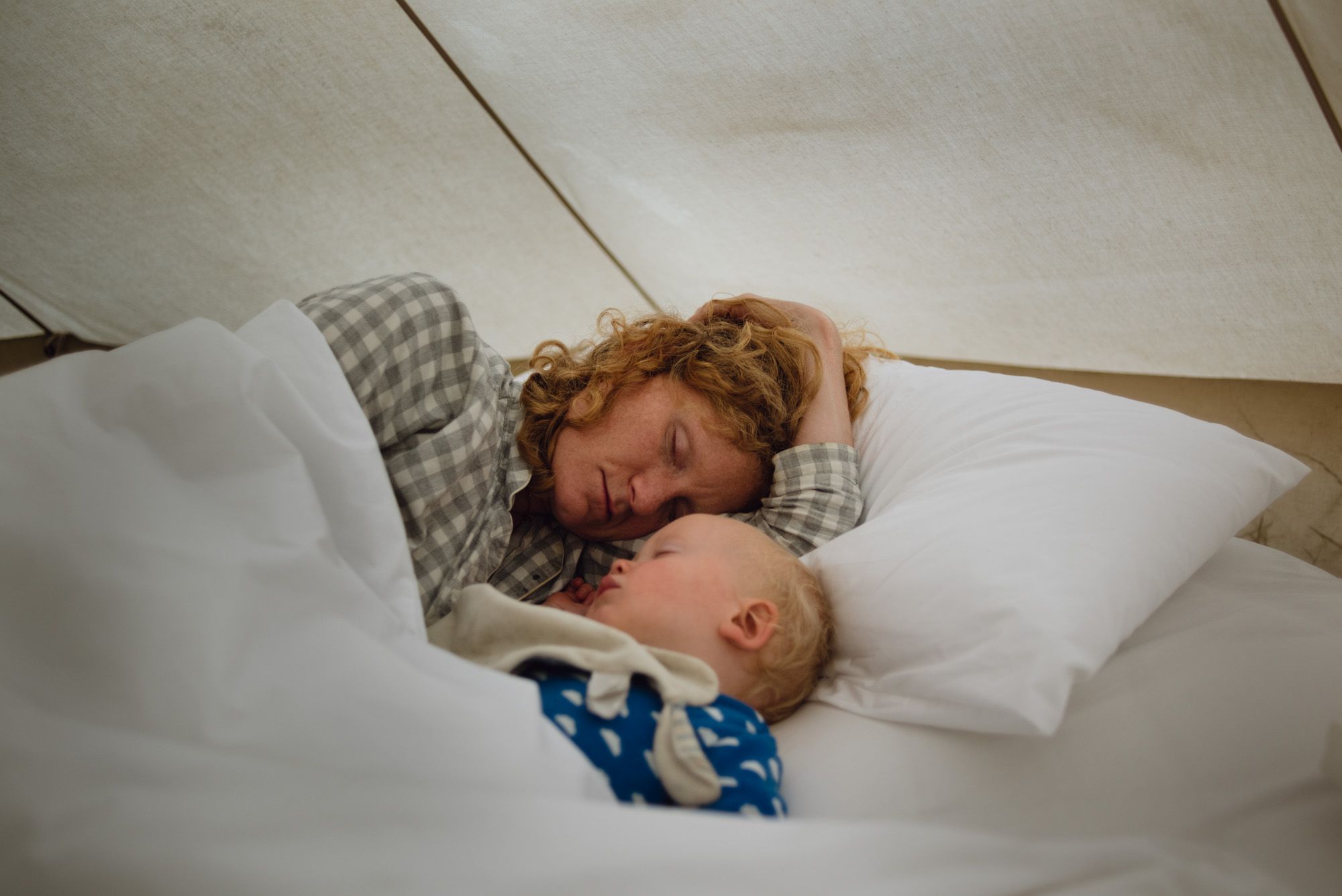 A woman and her young child asleep in a canvas bell tent.