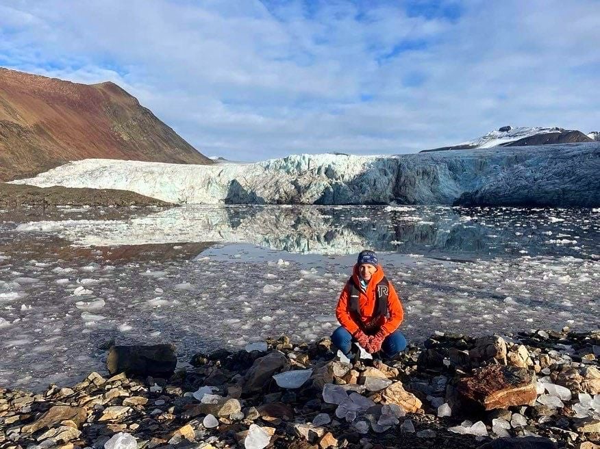 Expedition medic Sophie Redlin poses in front of a glacier in the Arctic.