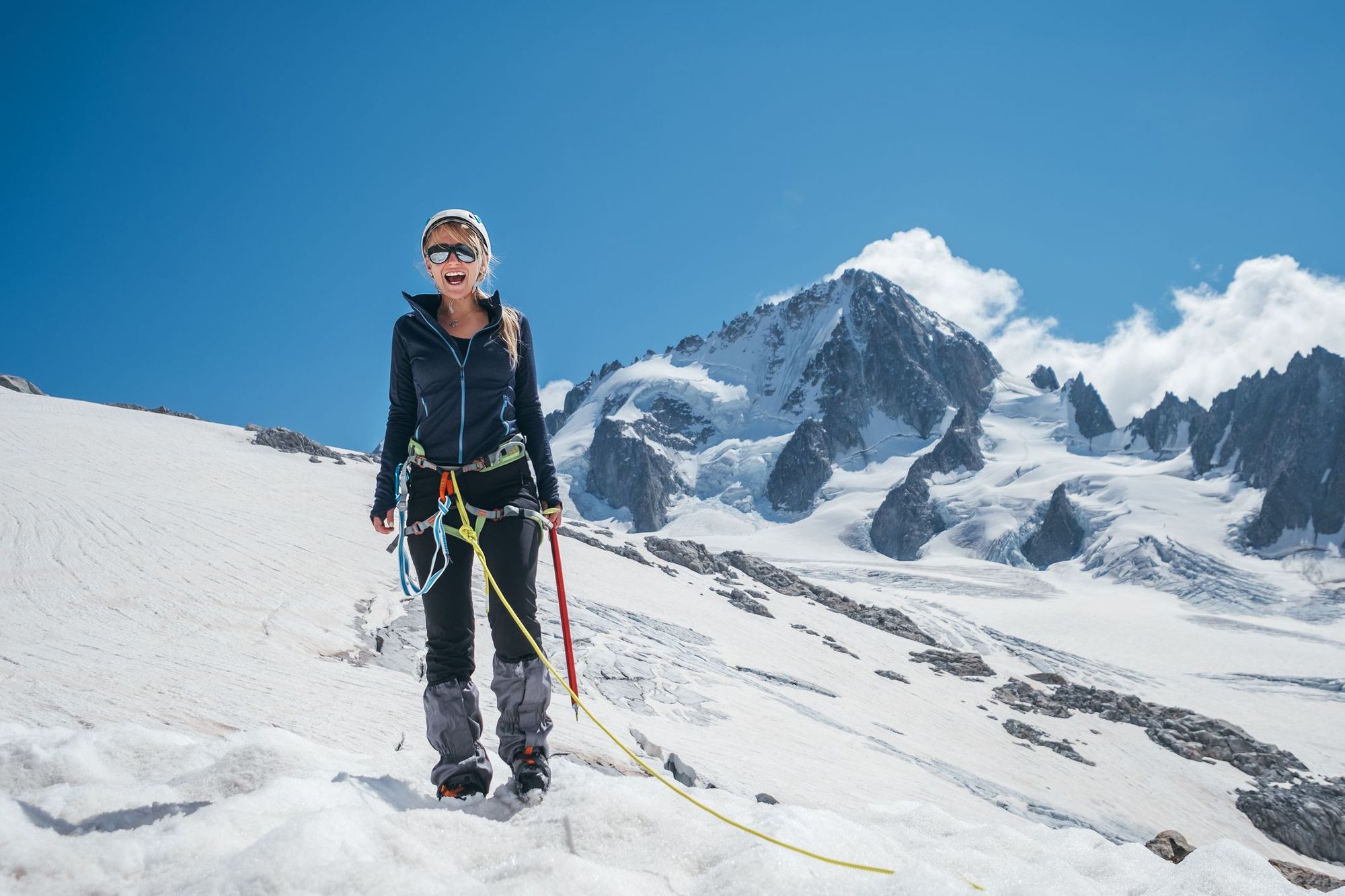 A female mountaineer stands out in the open in front of a mountain in the snow