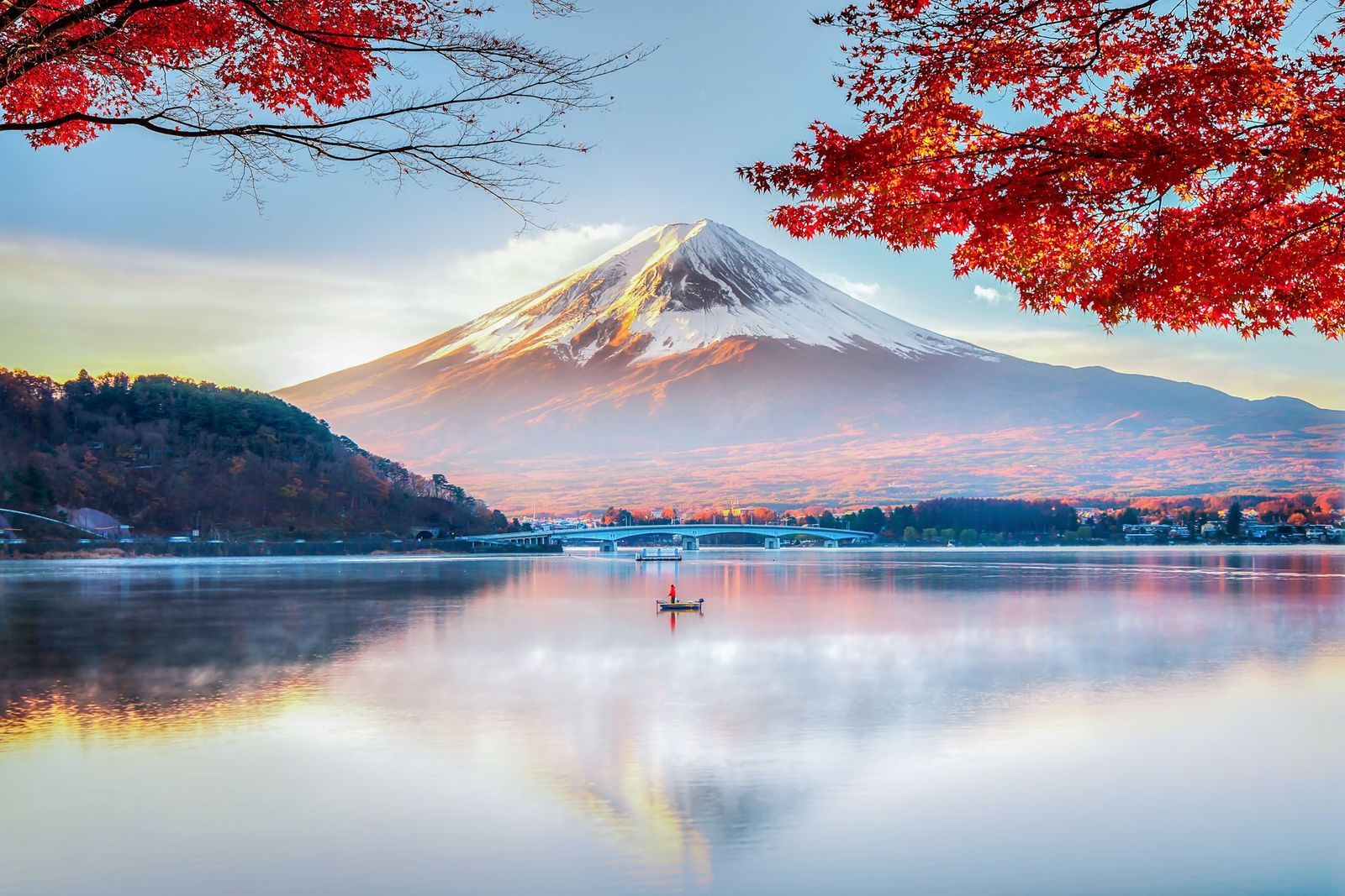 The snow-capped, symmetrical summit of Mount Fuji, Japan, at sunrise, with a lake in the foreground.