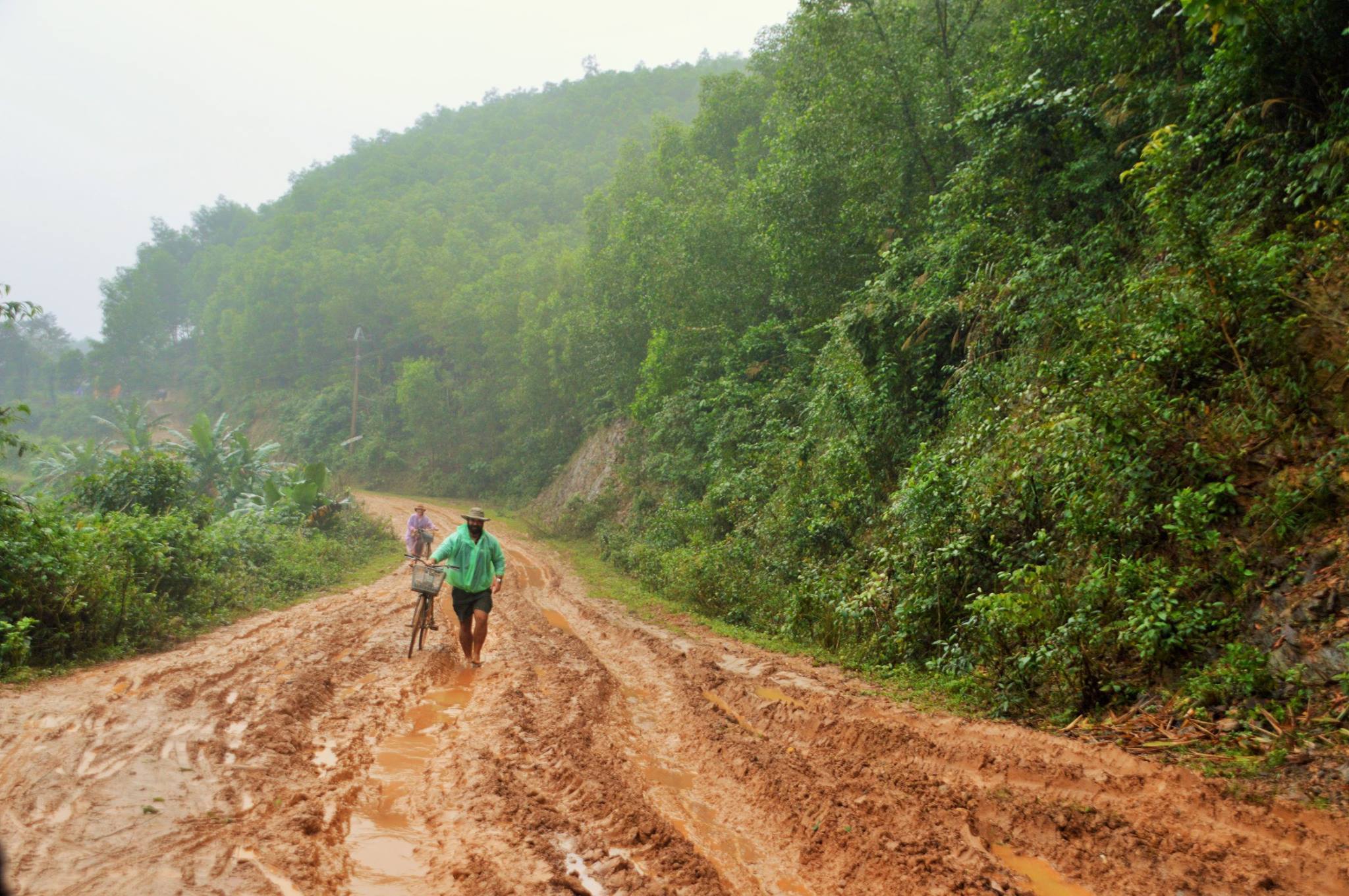 Two cyclists tramp through mud during Vietnam's rainy season