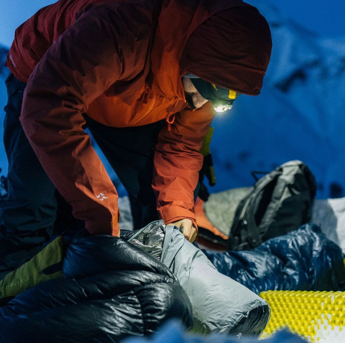 A man wearing a head torch pulls a tent out of a bag in the mountains.