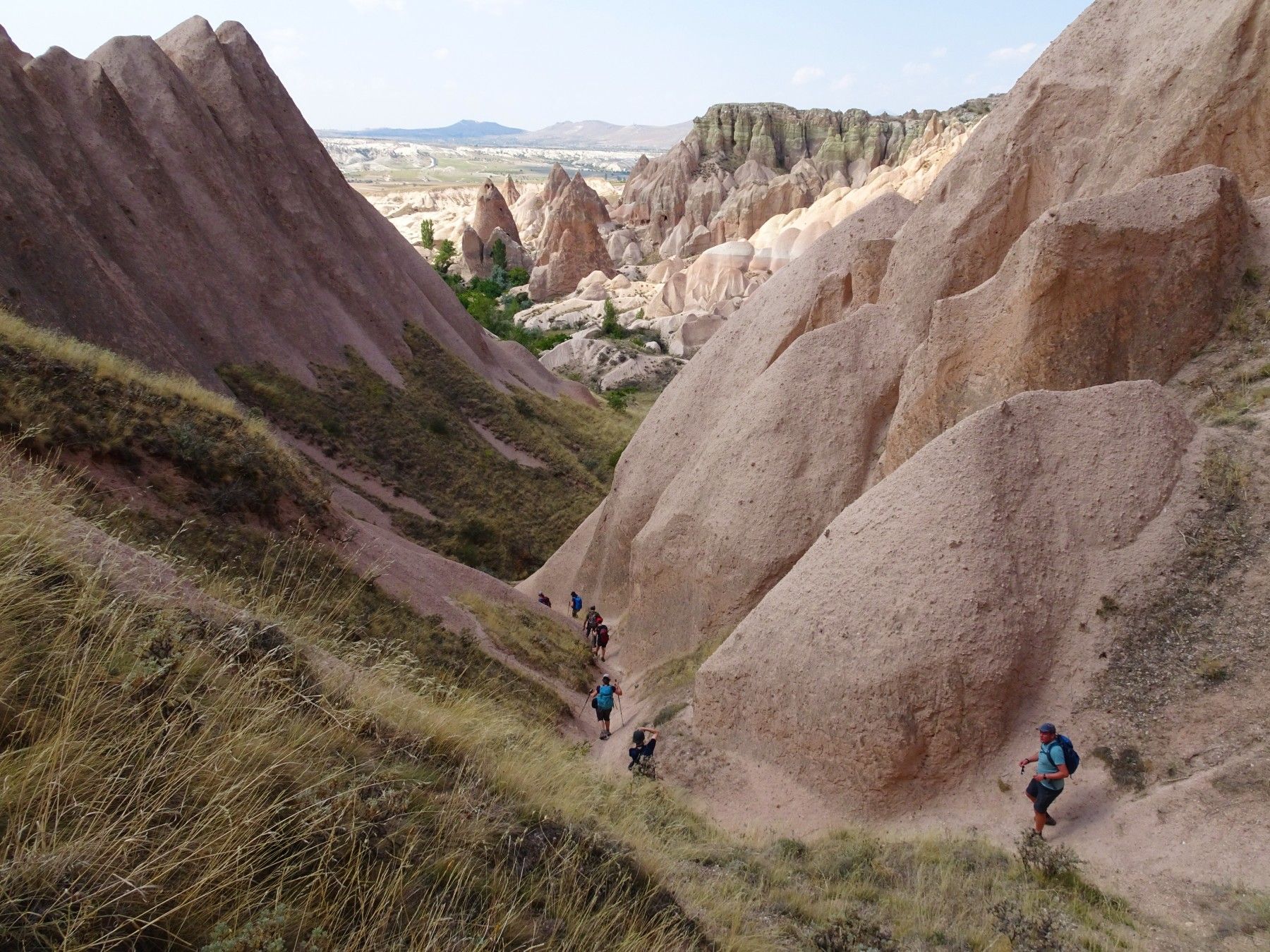 Hikers walk down a trail in Turkey's Cappadocia region, with the fairy chimneys on either side.