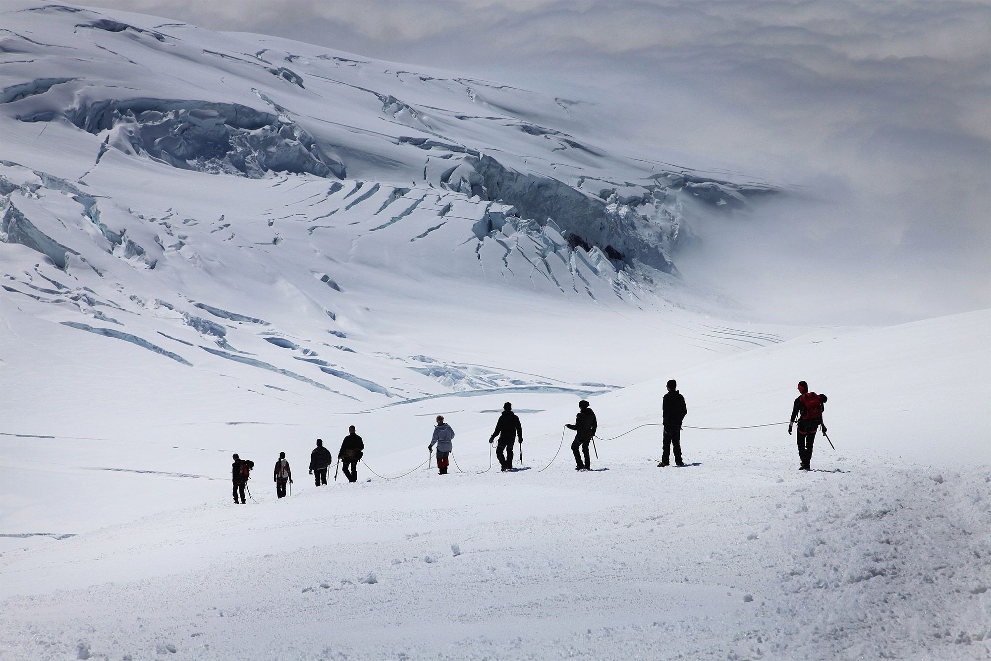 Climbers crossing the snowy mountains in Iceland, while roped together.