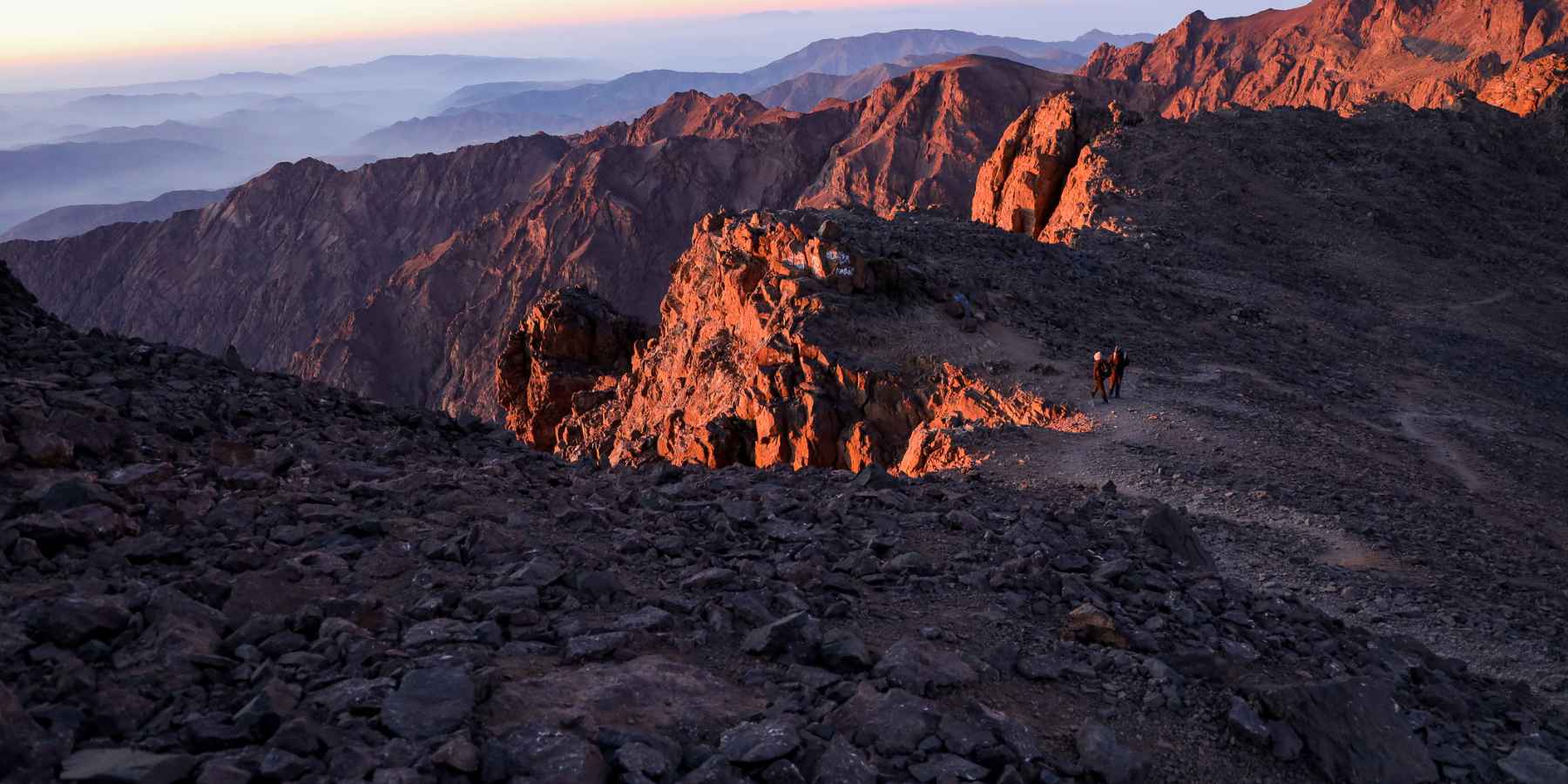 Two hikers watch the sun rise in the rocky High Atlas Mountains of Morocco.