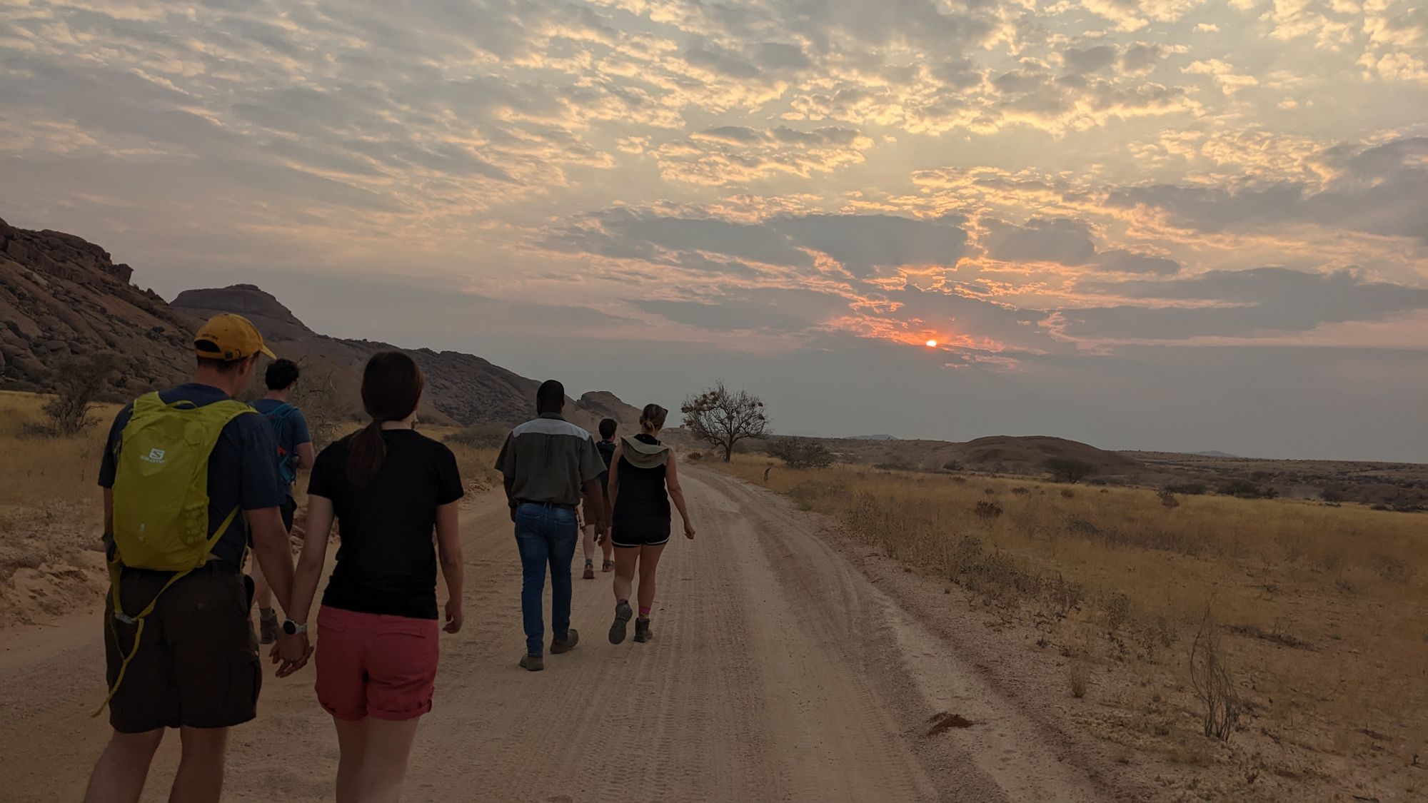 Hikers walking along a dusty road at sunrise.