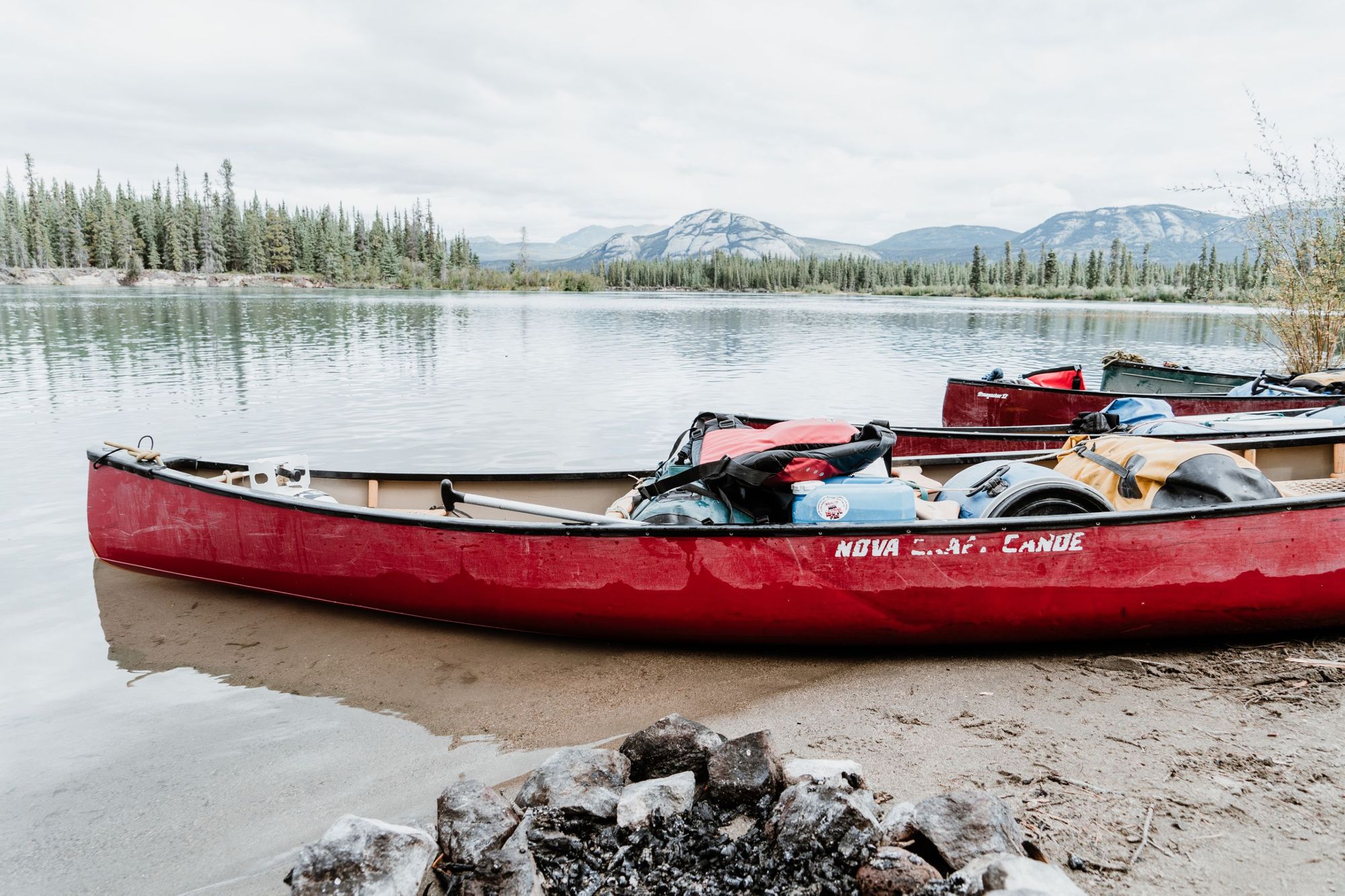 A loaded canoe on the Yukon River, with hills and forest in the background.