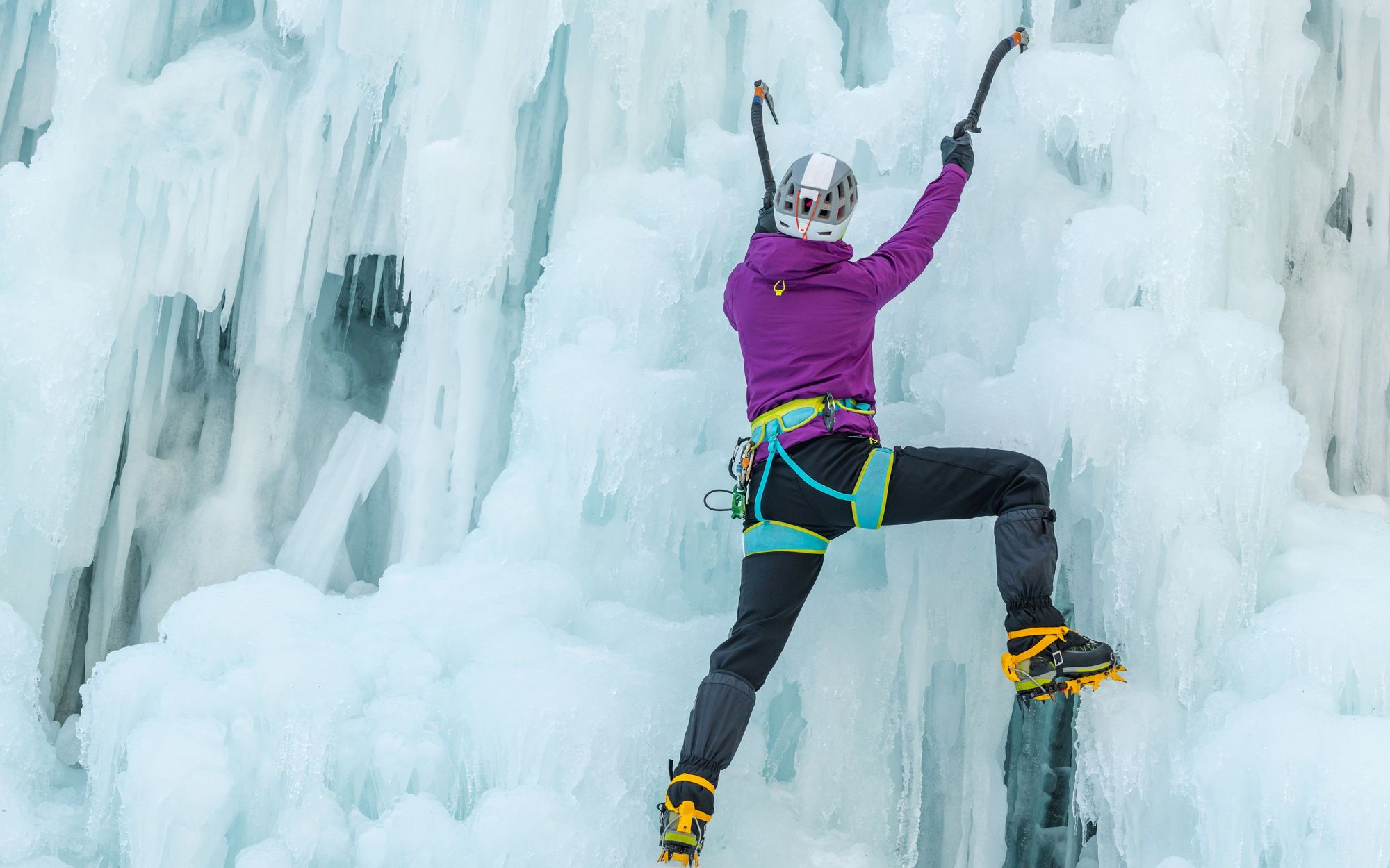 A woman climbs a frozen waterfall, using ice axes.
