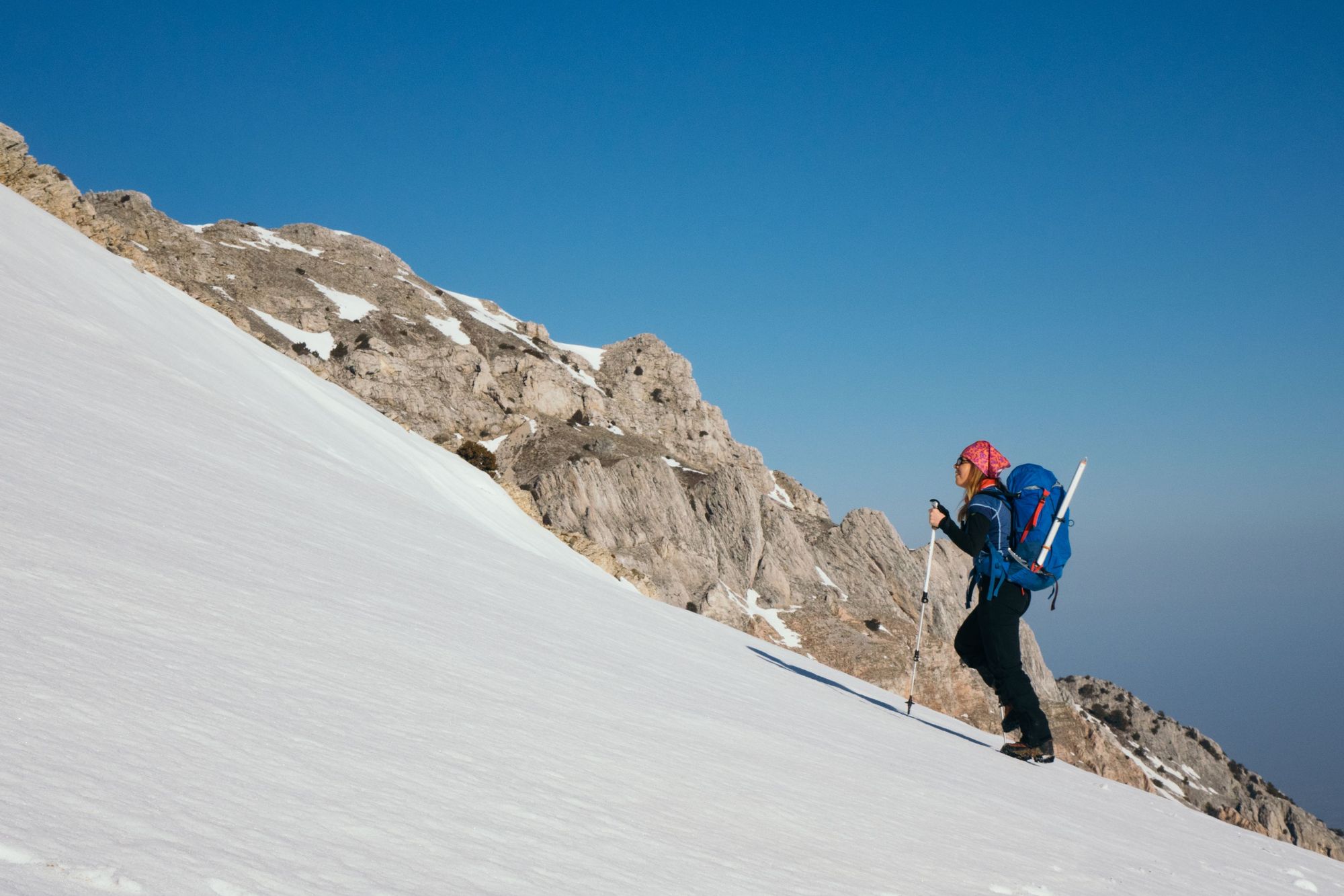 A woman climbs a mountain with a walking pole and ice axe.