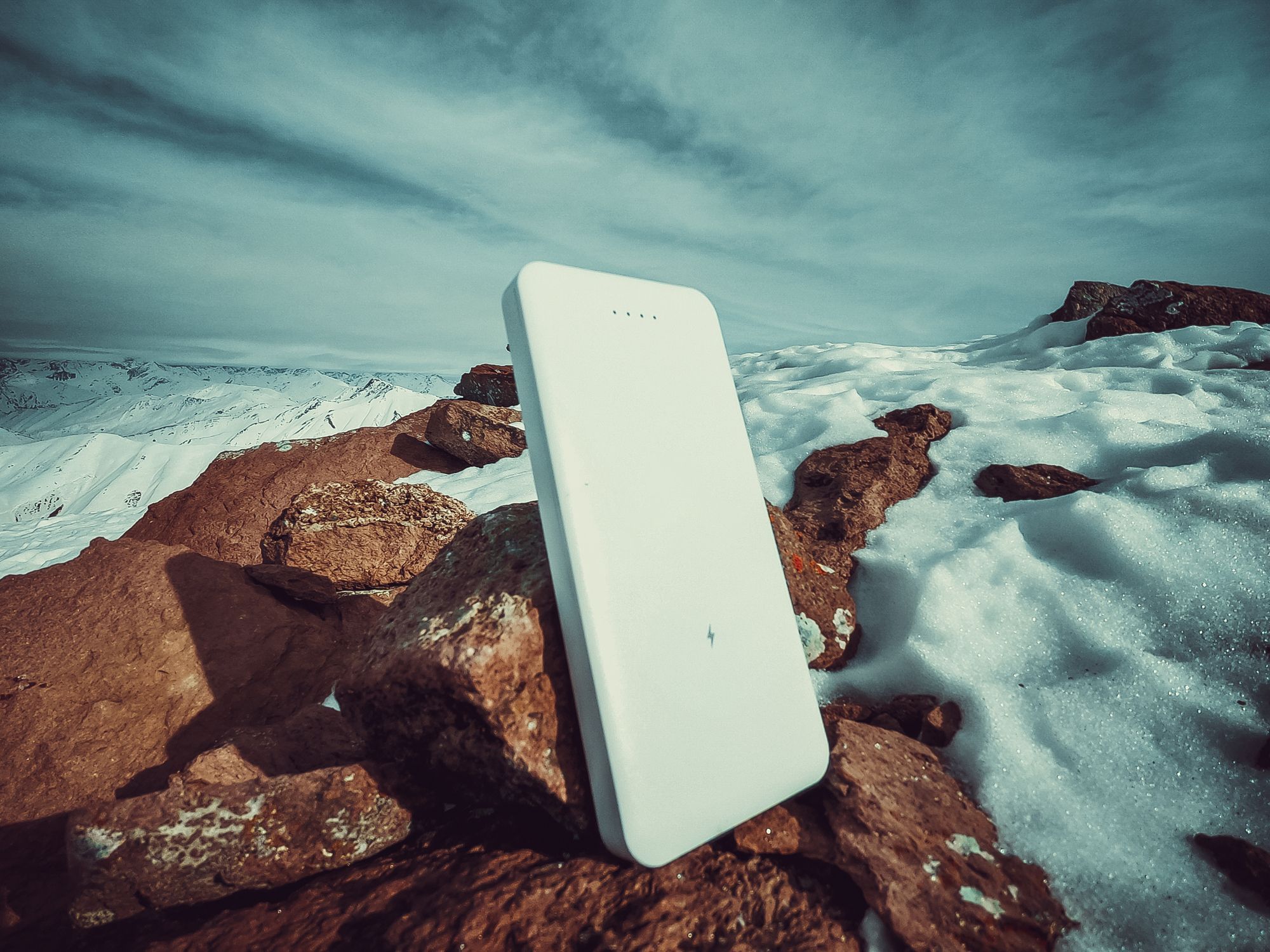 A power bank placed on exposed rock, surrounded by snow.