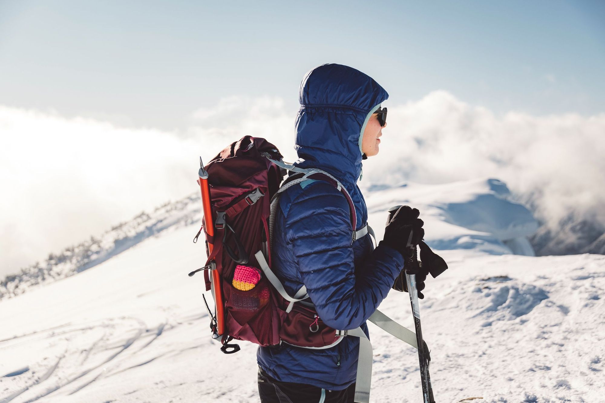 A hiker wearing a down jacket and a back pack, surrounded by snow covered mountains.