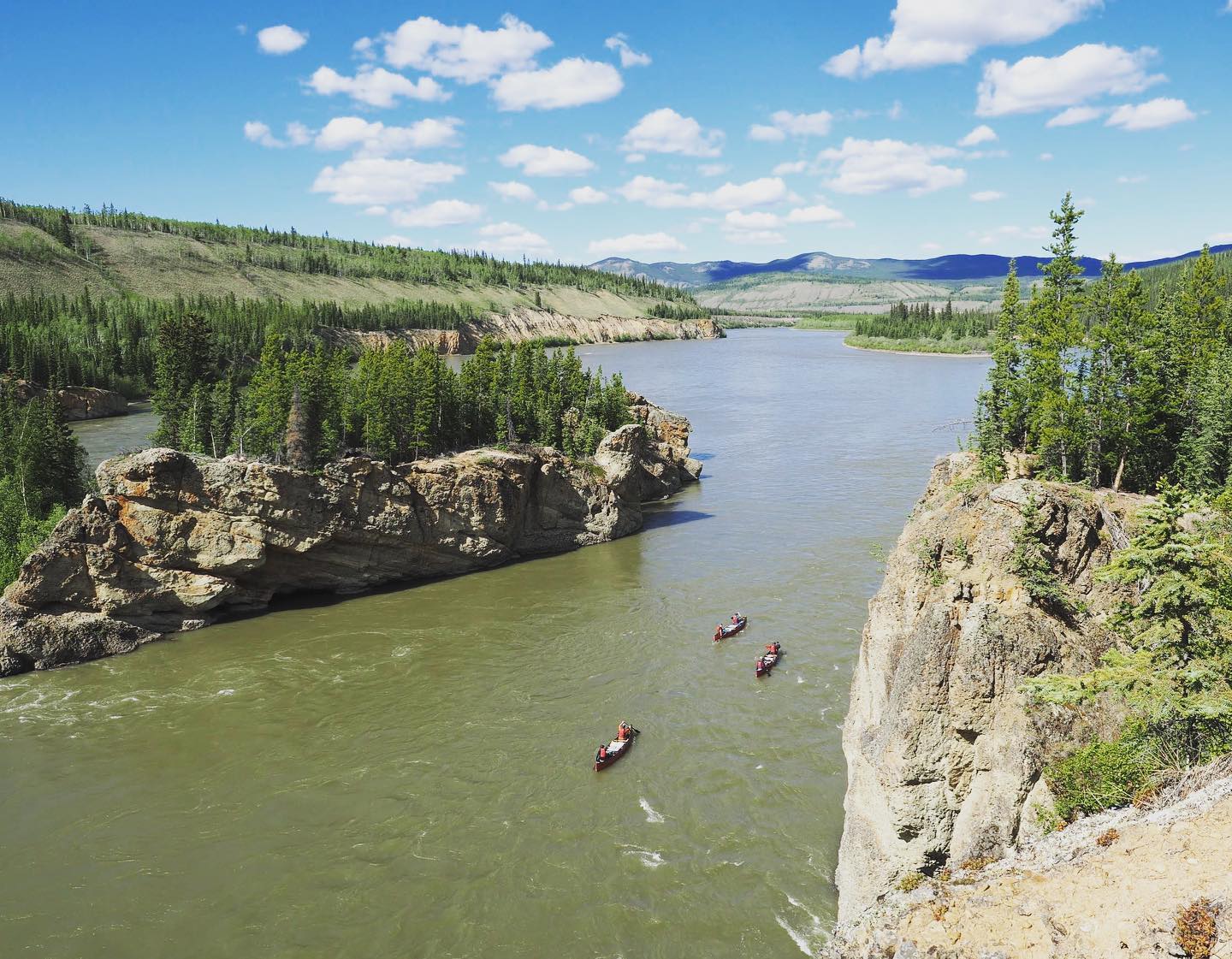 Three canoes drift down the Yukon River, Canada, surrounded by limestone cliffs.