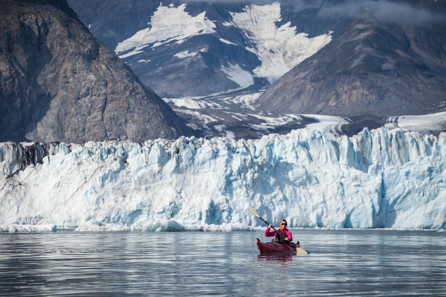 A woman kayaks in front of a glacier in Alaska.