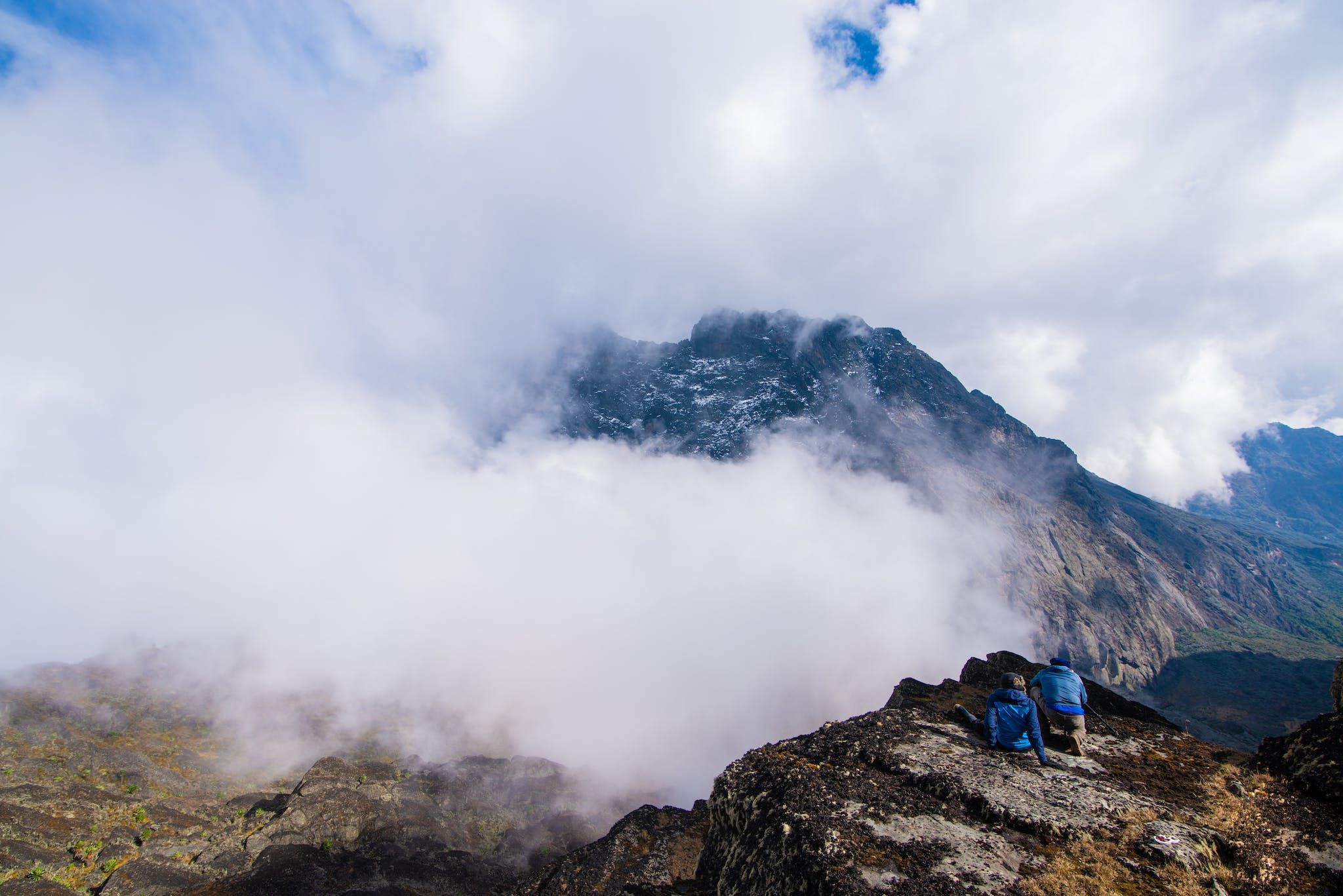 A pair of hikers look out on the vast Rwenzori mountain range, hidden behind a cloud of mist.