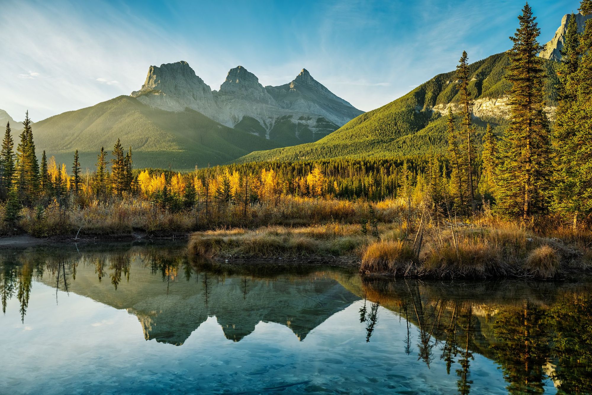 Sunrise over the Three Sisters, reflecting in Policeman Creek, Canmore, Alberta. Photo: Getty