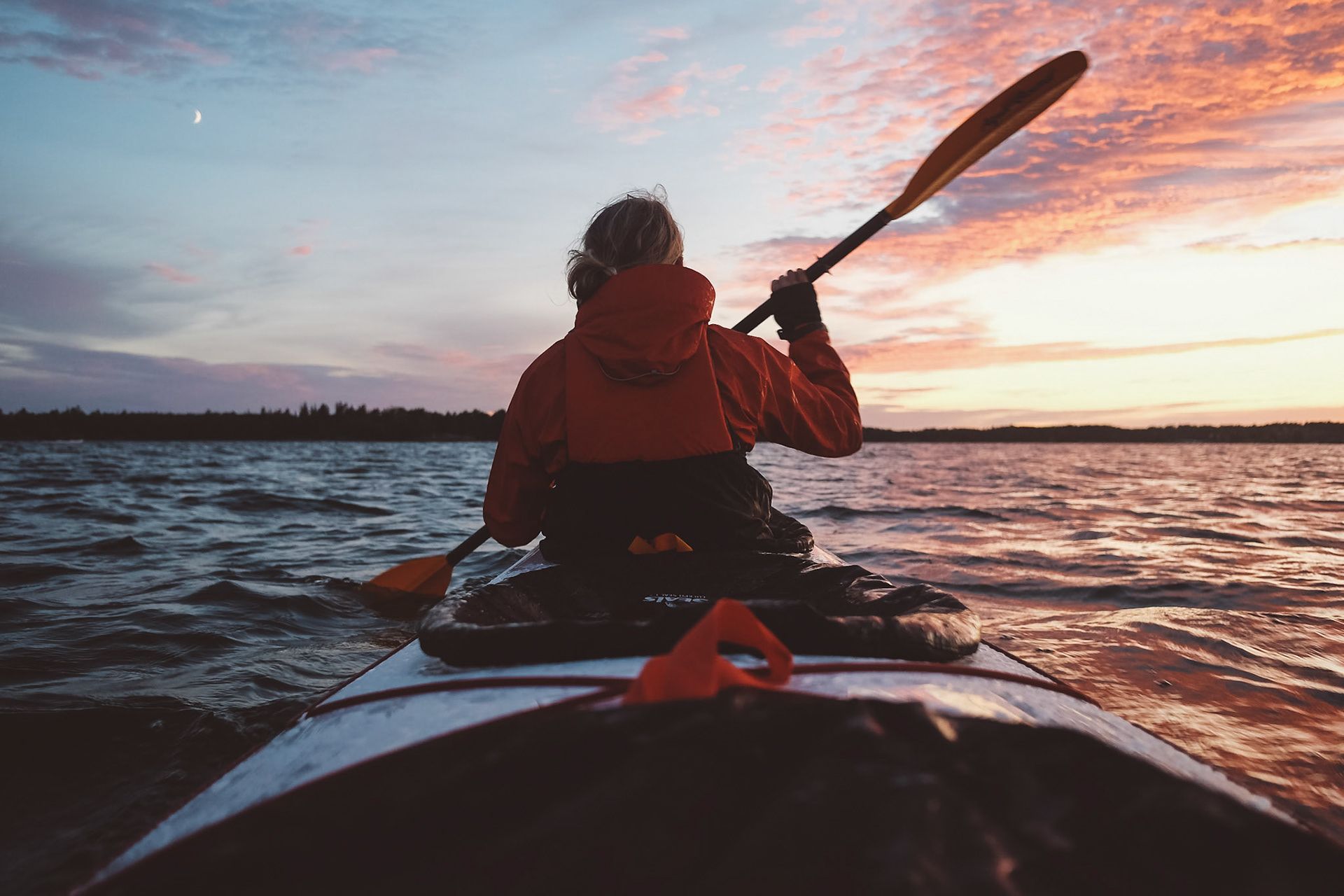 A kayaker paddling across the water as the sun sets.