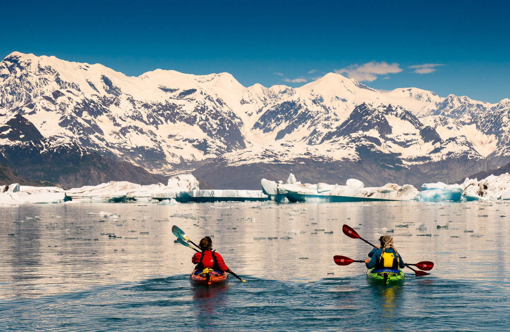 Kayakers paddling towards icebergs in Alaska.
