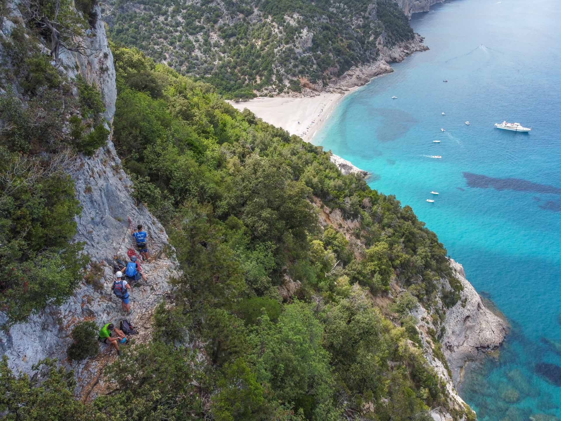 Hikers roped together on the Selvaggio Blue trail, Sardinia, as they negotiate a rocky cliff.