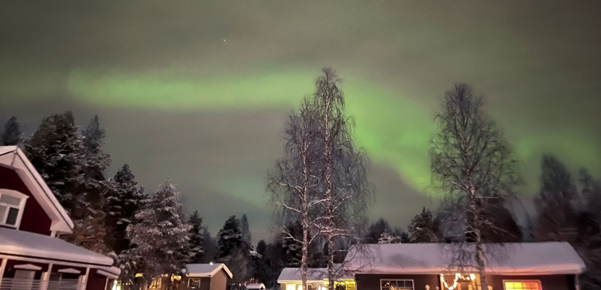 The northern lights above forest and cabins, Finland.