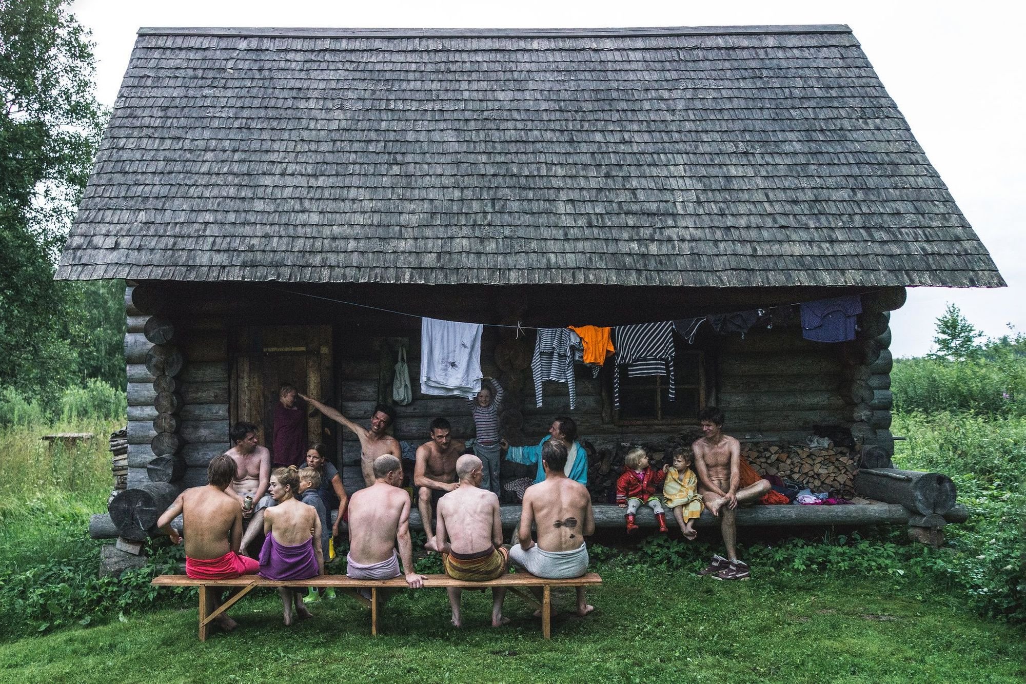 A group of men and women in Estonia sit outside a traditional smoke sauna.