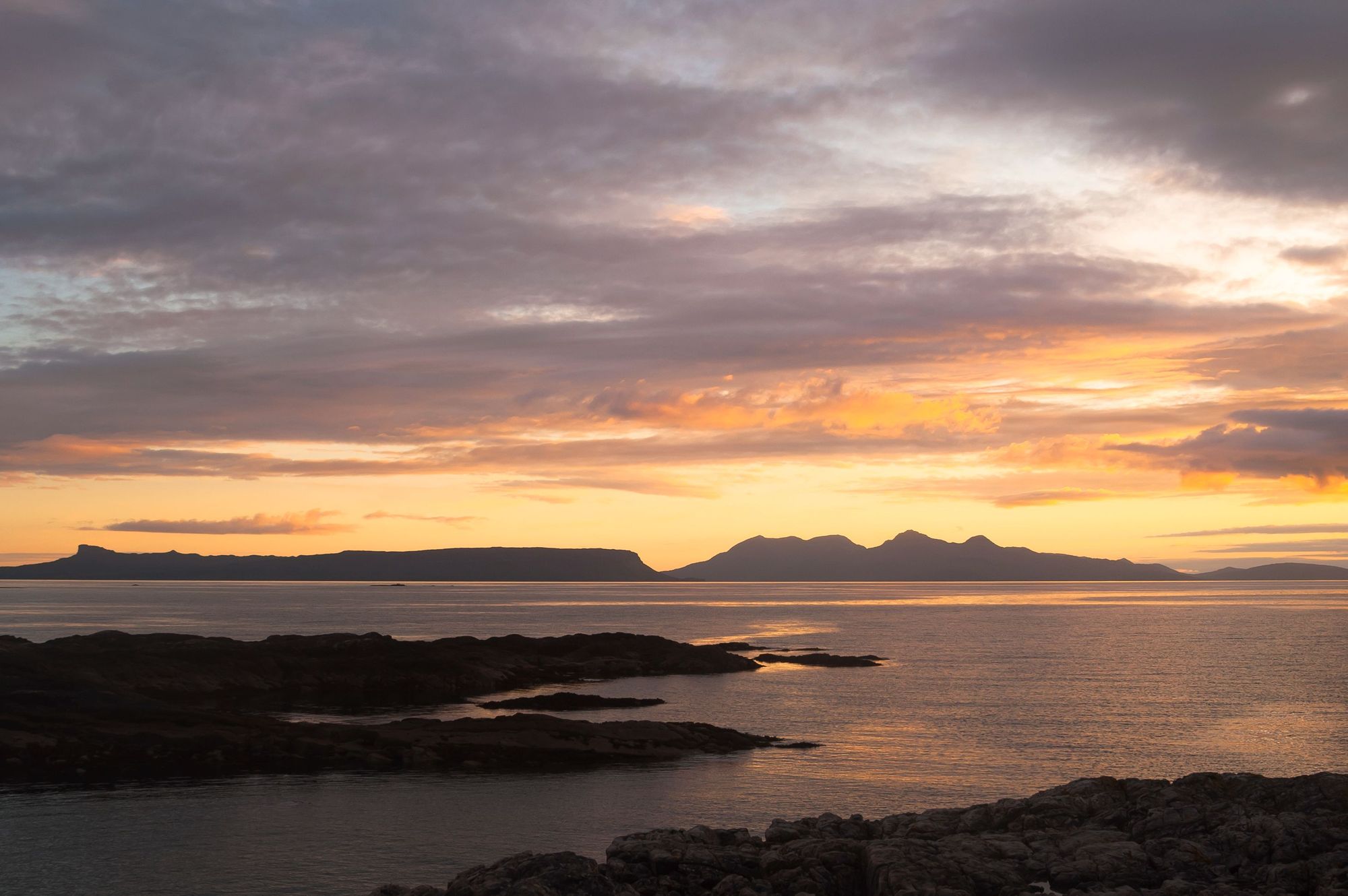 The dorsal fin and outline of Eigg, left, and the mountainous ridgeline of the Rum Cuillin, right, as the sun sets. Photo: Getty