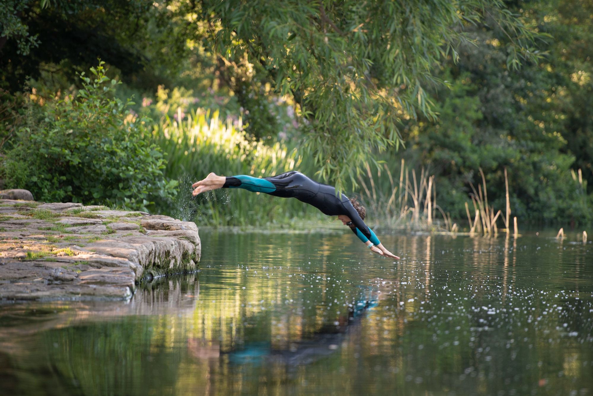 A woman in a wetsuit dives into a river.