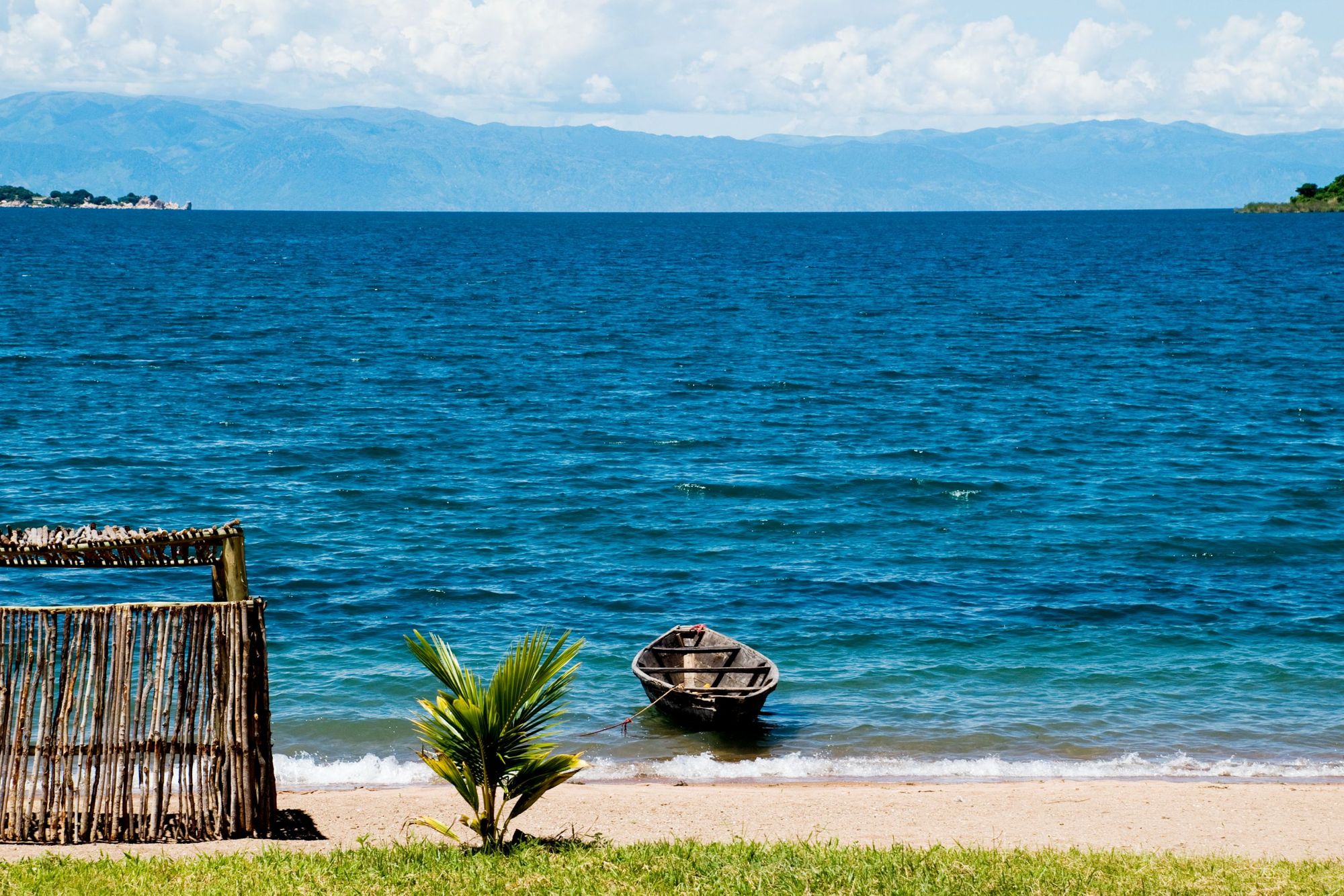 A wooden boat floats on the shores of Lake Tanganyika, looking out over the lapping water. Photo: Getty
